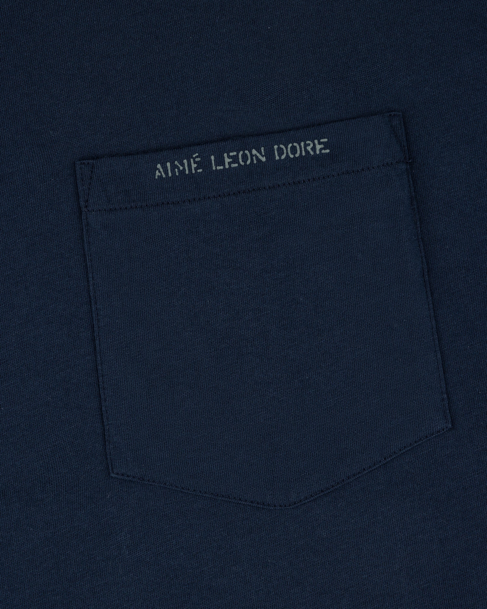 Close-up of the Jacquard Collar Pocket Tee, featuring a navy blue pocket and AIME LEON DORE text above it.