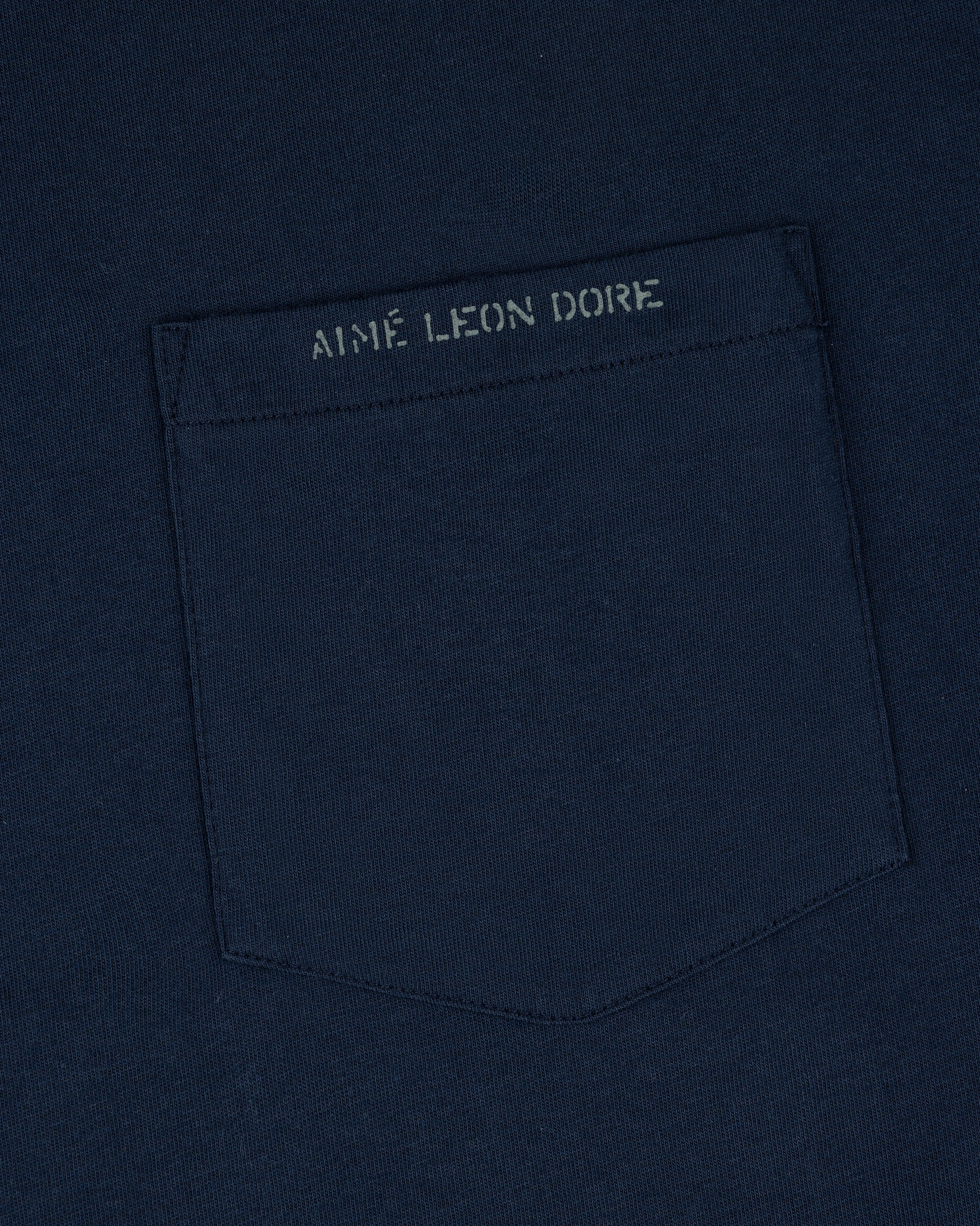 Close-up of the Jacquard Collar Pocket Tee, featuring a navy blue pocket and AIME LEON DORE text above it.