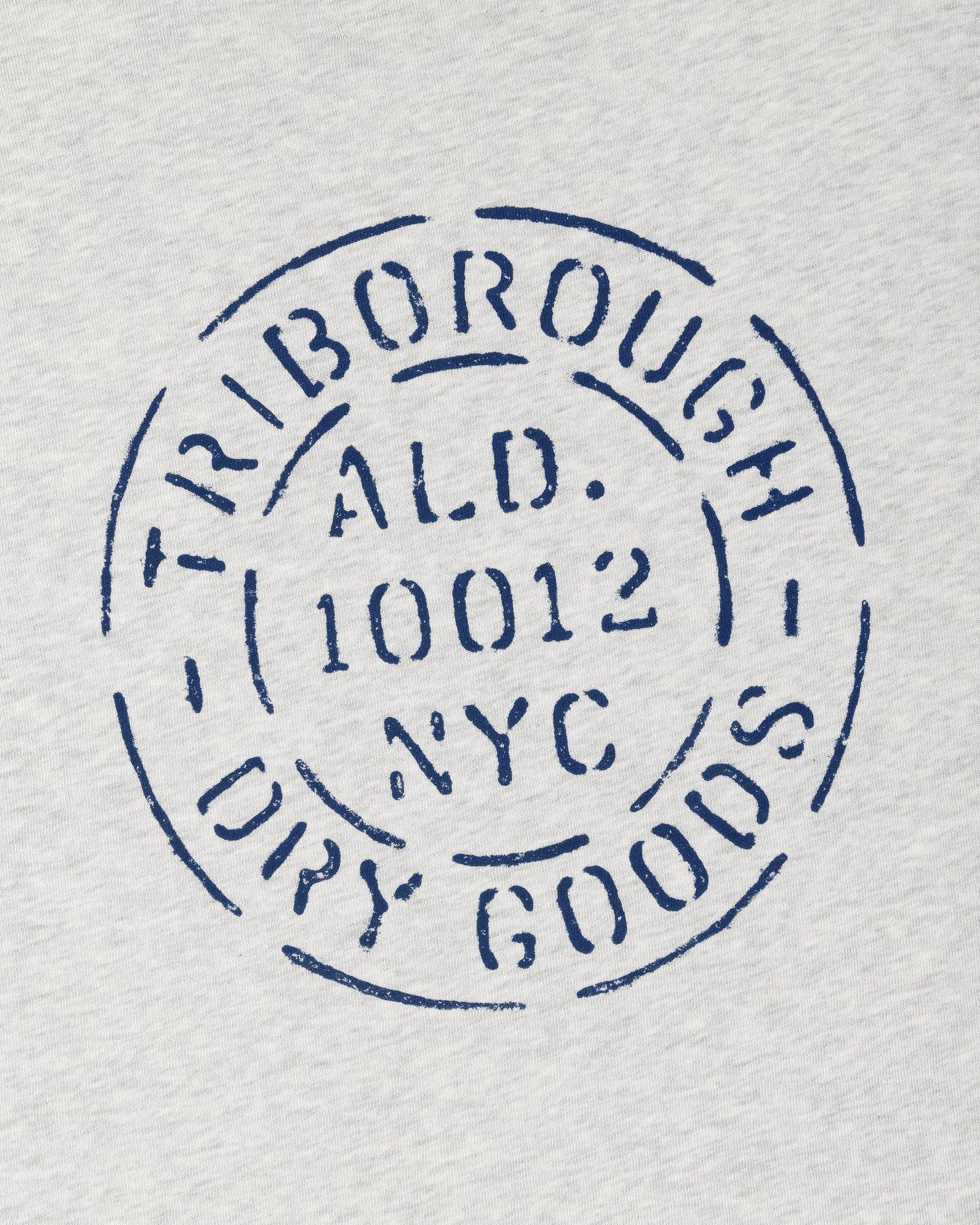 Circular blue “TRIBOROUGH DRY GOODS ALD. 10012 NYC” stamp on light gray Triborough Dry Goods Pocket Tee.