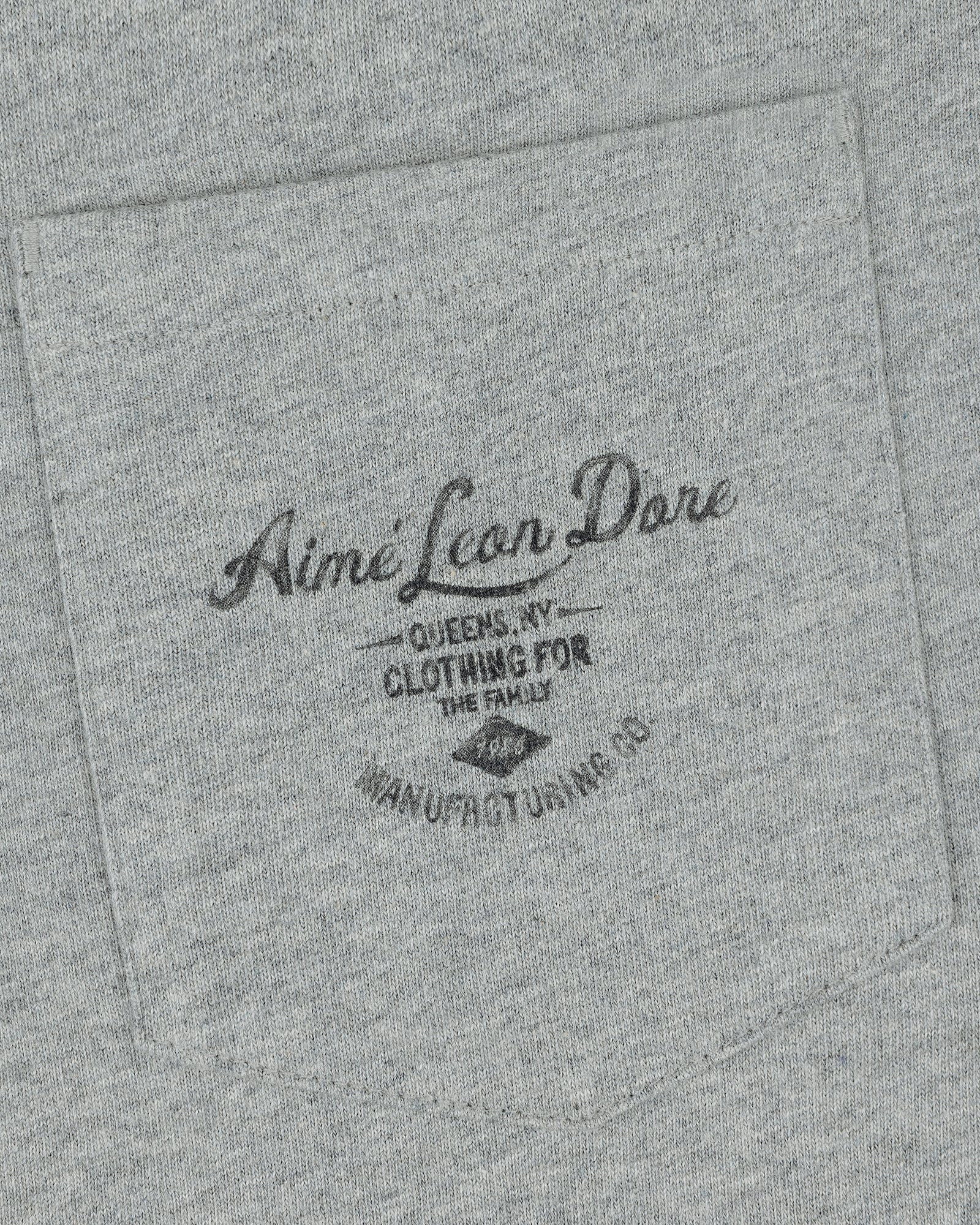 Gray fabric pocket on the General Store Pocket Tee with black text: Aimé Leon Dore, Queens NY, Clothing for the Family.