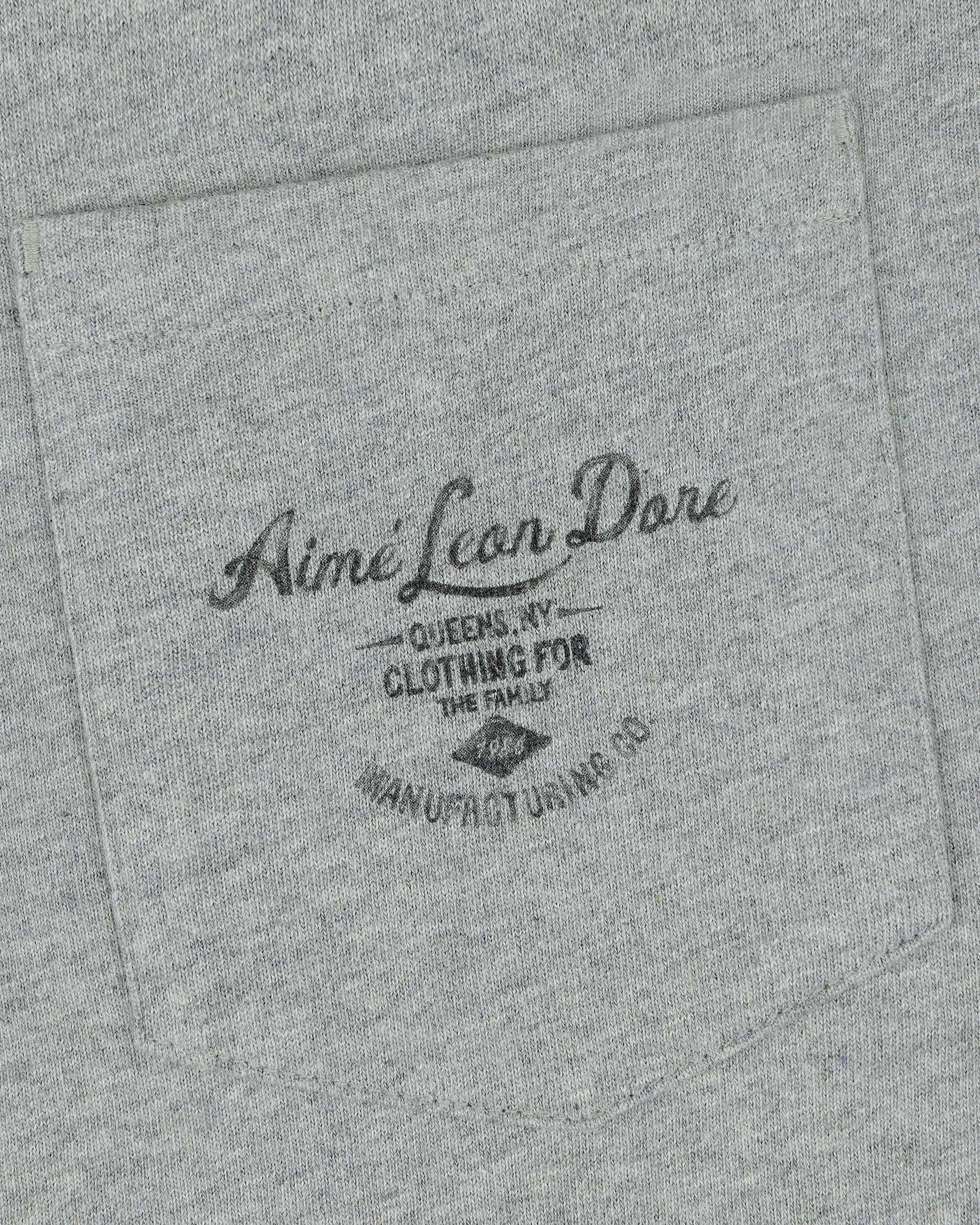 Gray fabric pocket on the General Store Pocket Tee with black text: Aimé Leon Dore, Queens NY, Clothing for the Family.