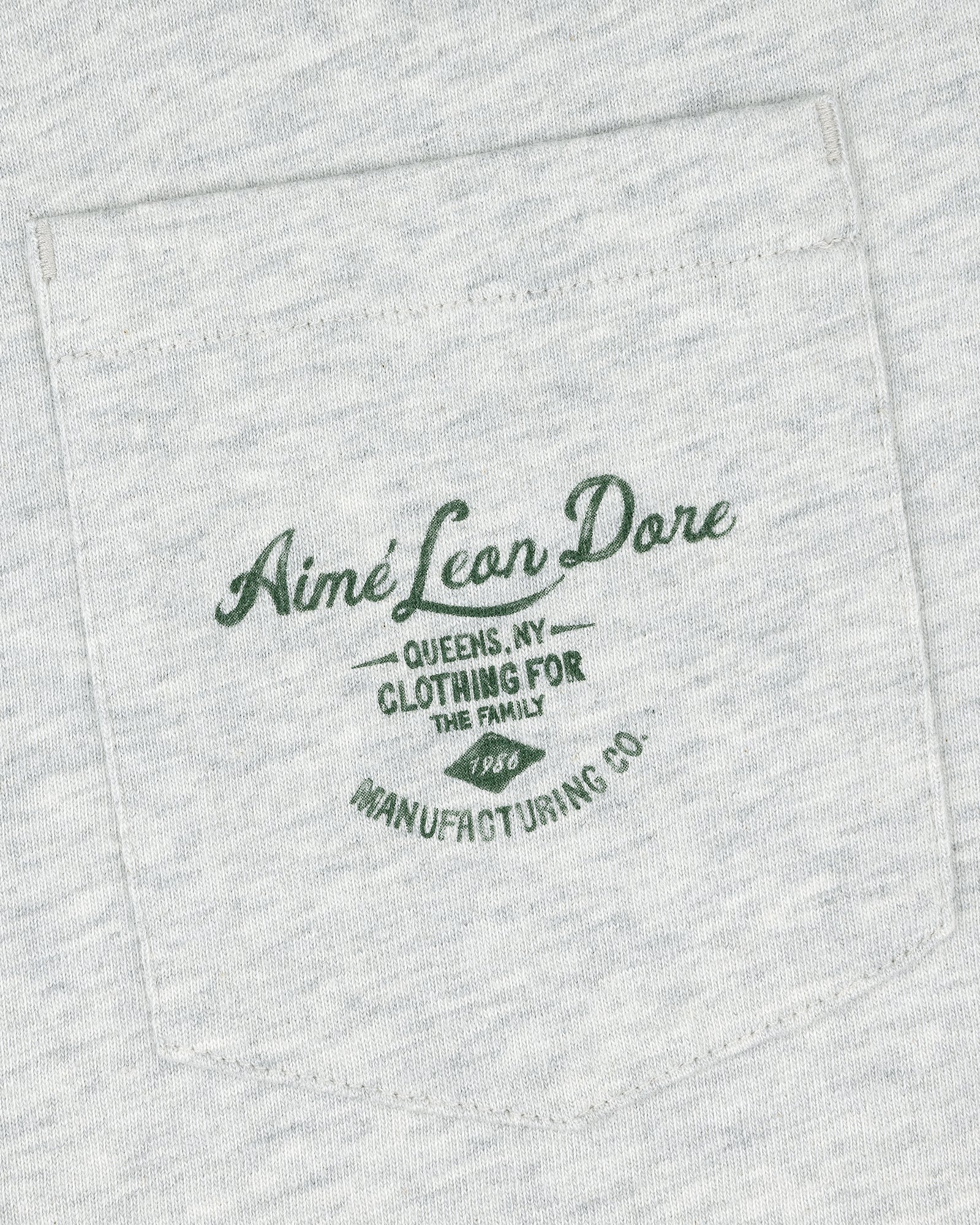 Light gray General Store Pocket Tee with dark green text: "Aimé Leon Dore Queens, NY Clothing For The Family 1986 Manufacturing Co.