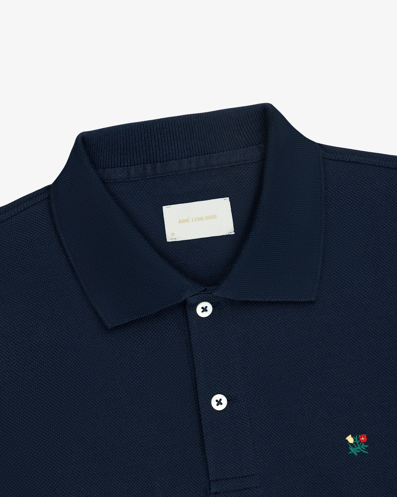 Long-Sleeve Crest Piqué Polo in navy blue with white buttons and a small flower chest embroidery, on white background.