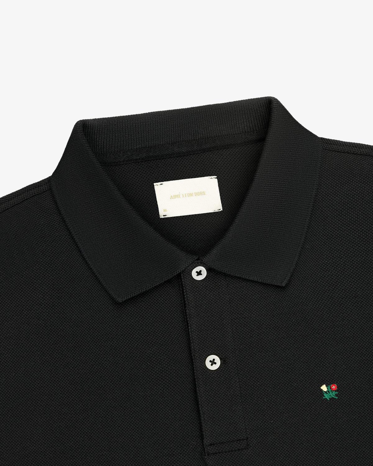Crest Piqué Polo: black, collared, two buttons, small flower logo embroidered on the chest.