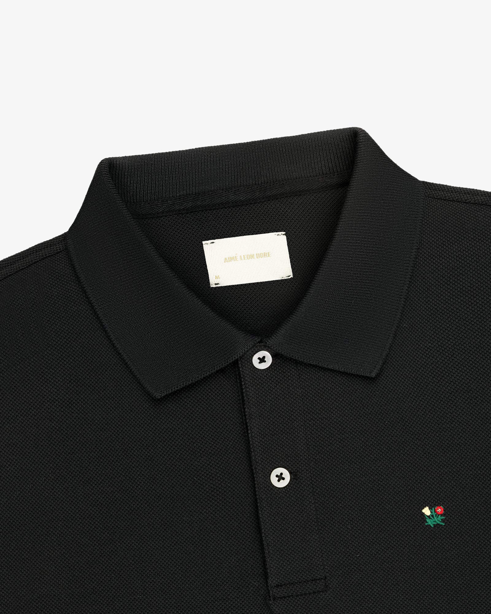 Crest Piqué Polo: black, collared, two buttons, small flower logo embroidered on the chest.