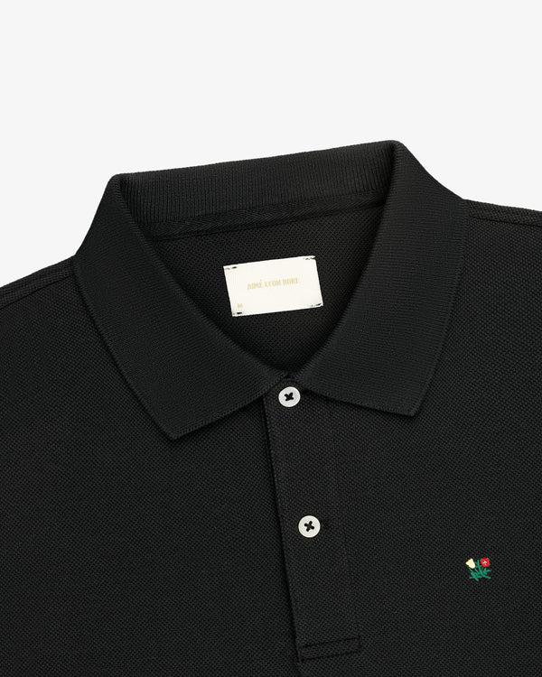 Crest Piqué Polo: black, collared, two buttons, small flower logo embroidered on the chest.