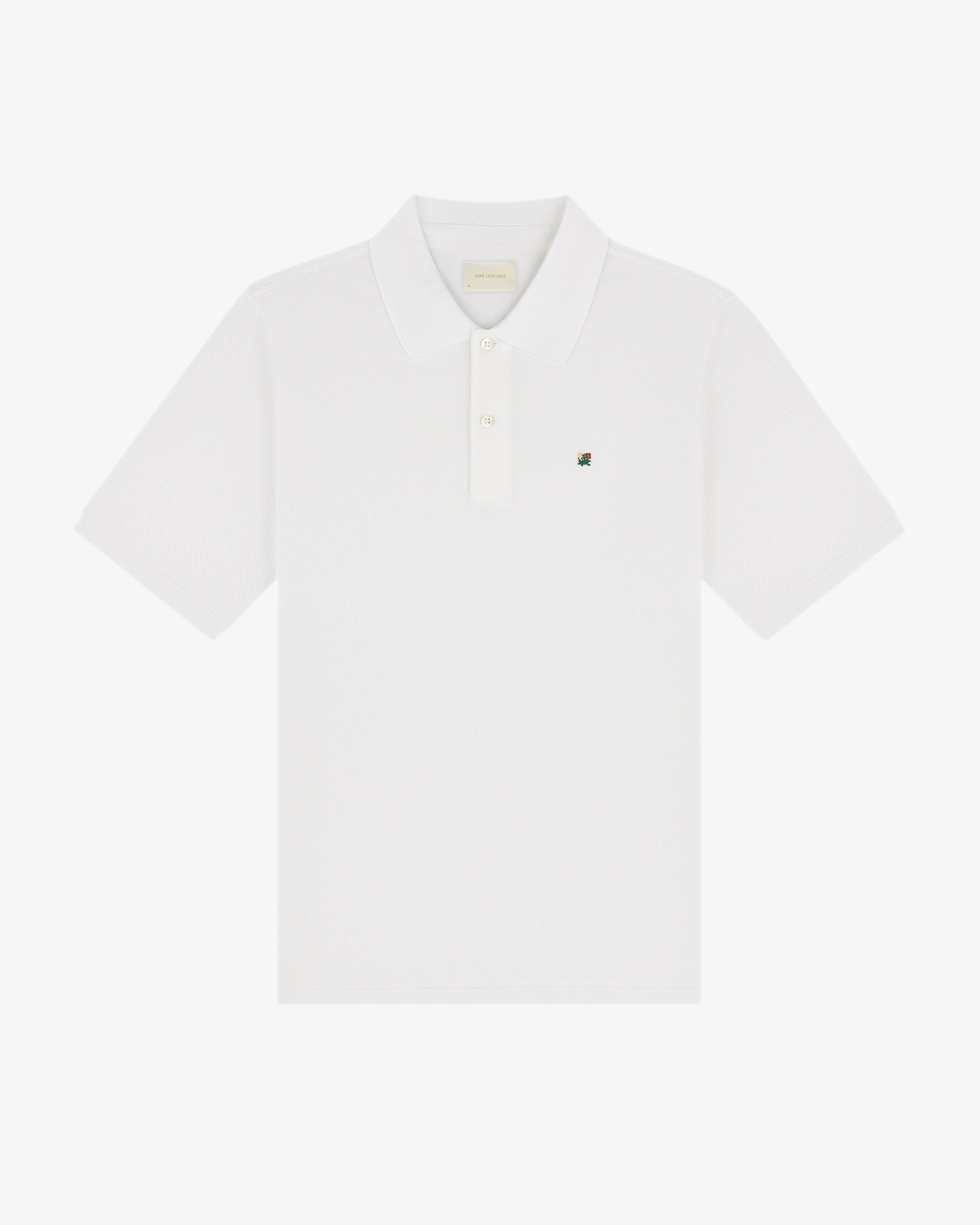 The Crest Piqué Polo is a white short-sleeve shirt with a collar and small embroidered logo on the left chest.
