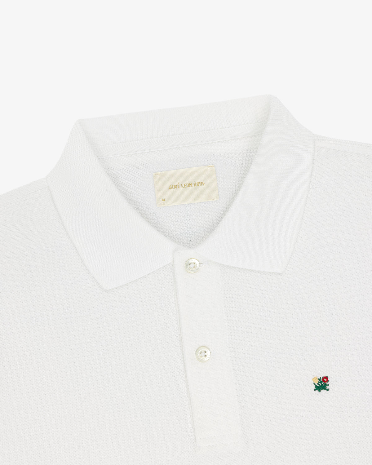 Crest Piqué Polo: White with a small green and red floral crest logo and two-button placket.