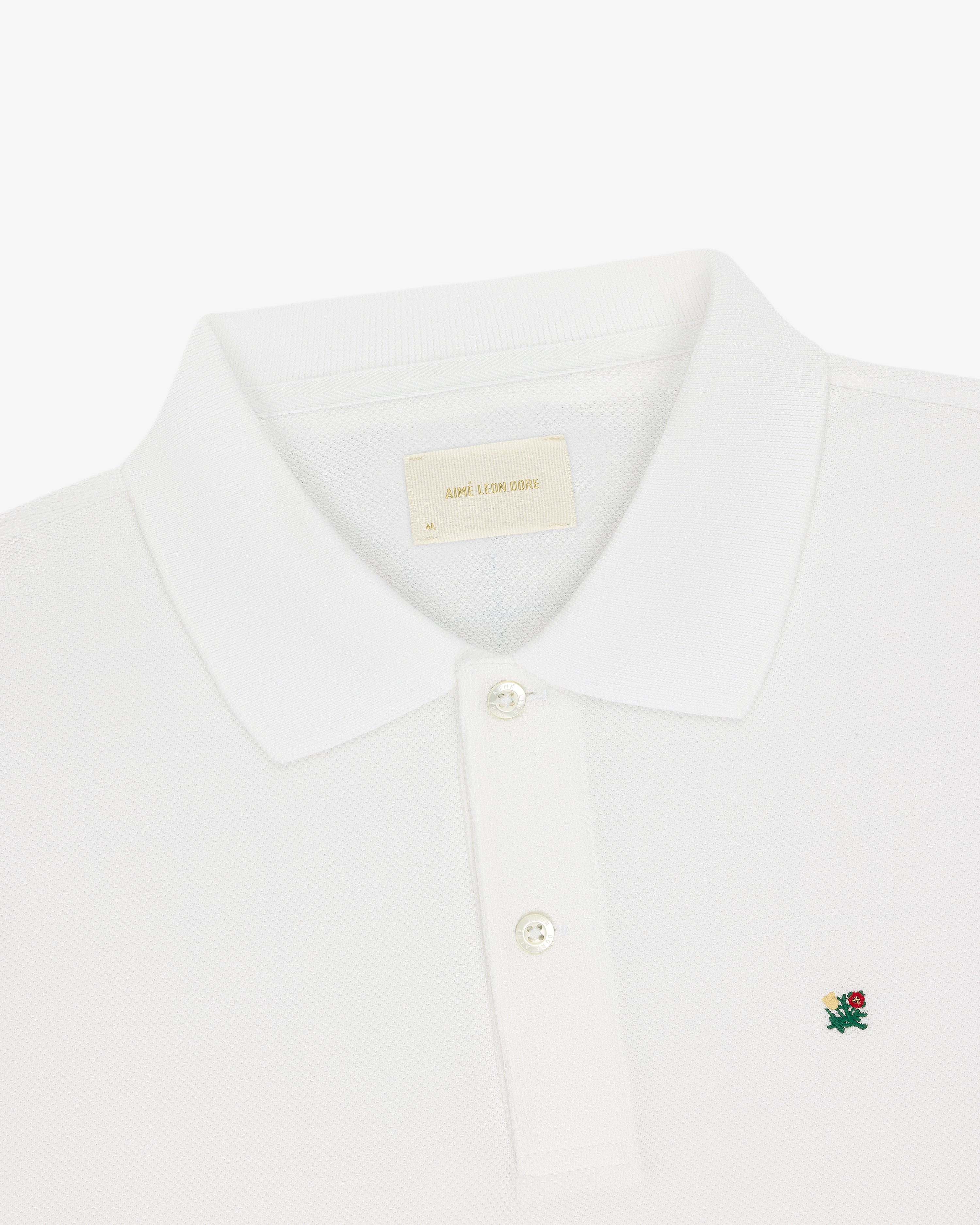 Crest Piqué Polo: White with a small green and red floral crest logo and two-button placket.
