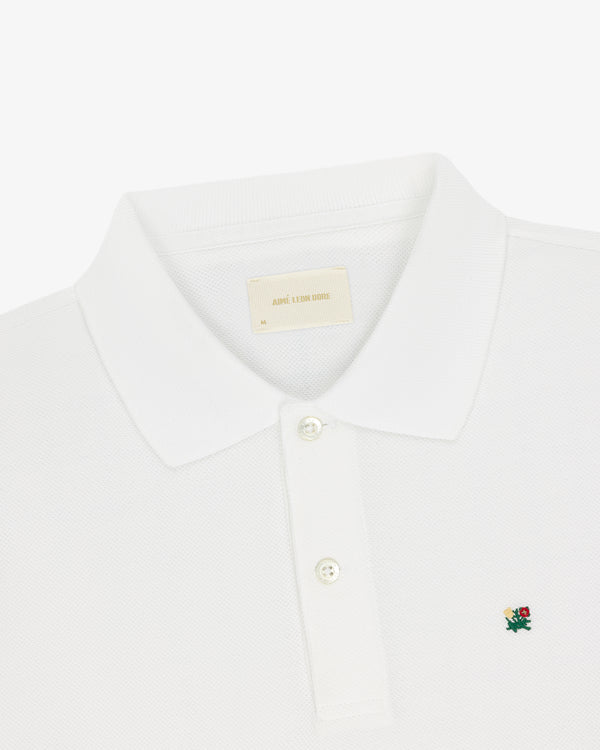 Crest Piqué Polo: White with a small green and red floral crest logo and two-button placket.