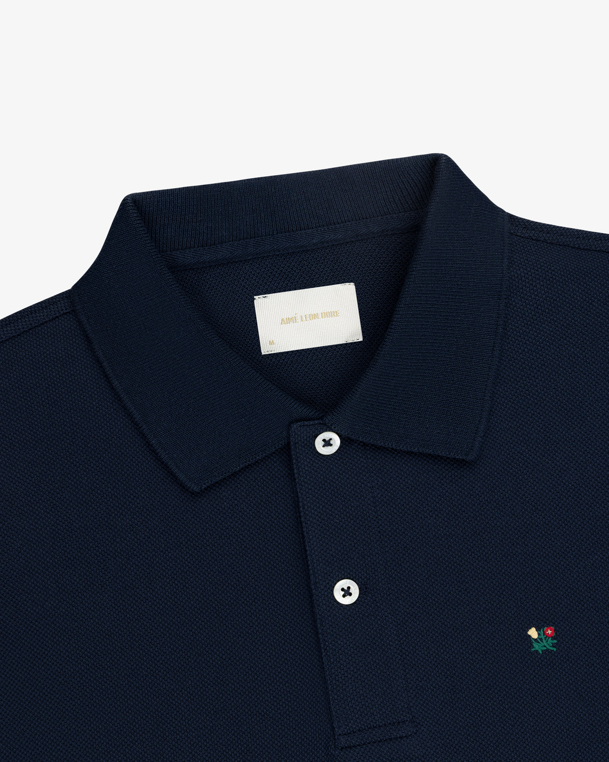 Crest Piqué Polo in navy blue with a small embroidered flower and two-button placket, shown on a white background.