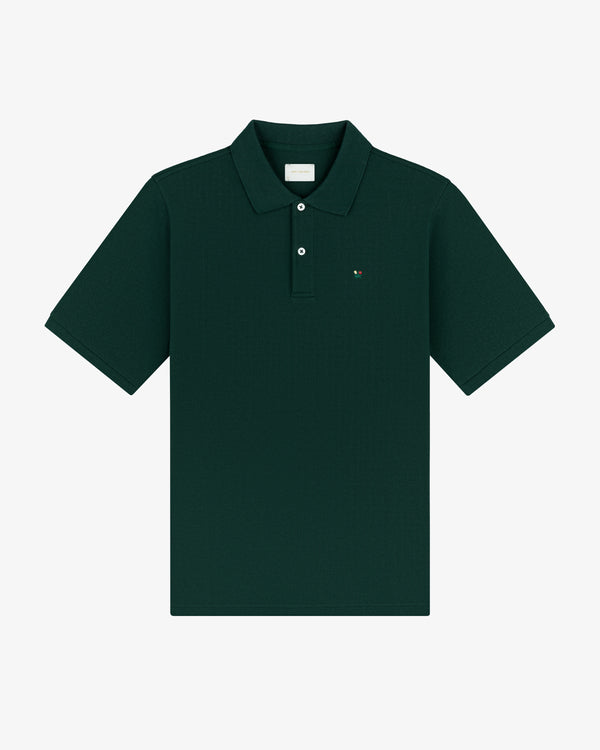 Crest Piqué Polo in dark green, short sleeves, collared with buttons, and a small chest logo, laid flat.
