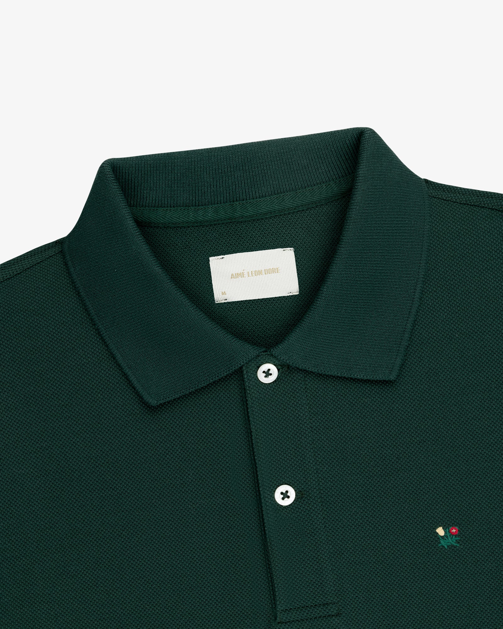 Crest Piqué Polo in dark green with a collar, two white buttons, and red & yellow chest embroidery.