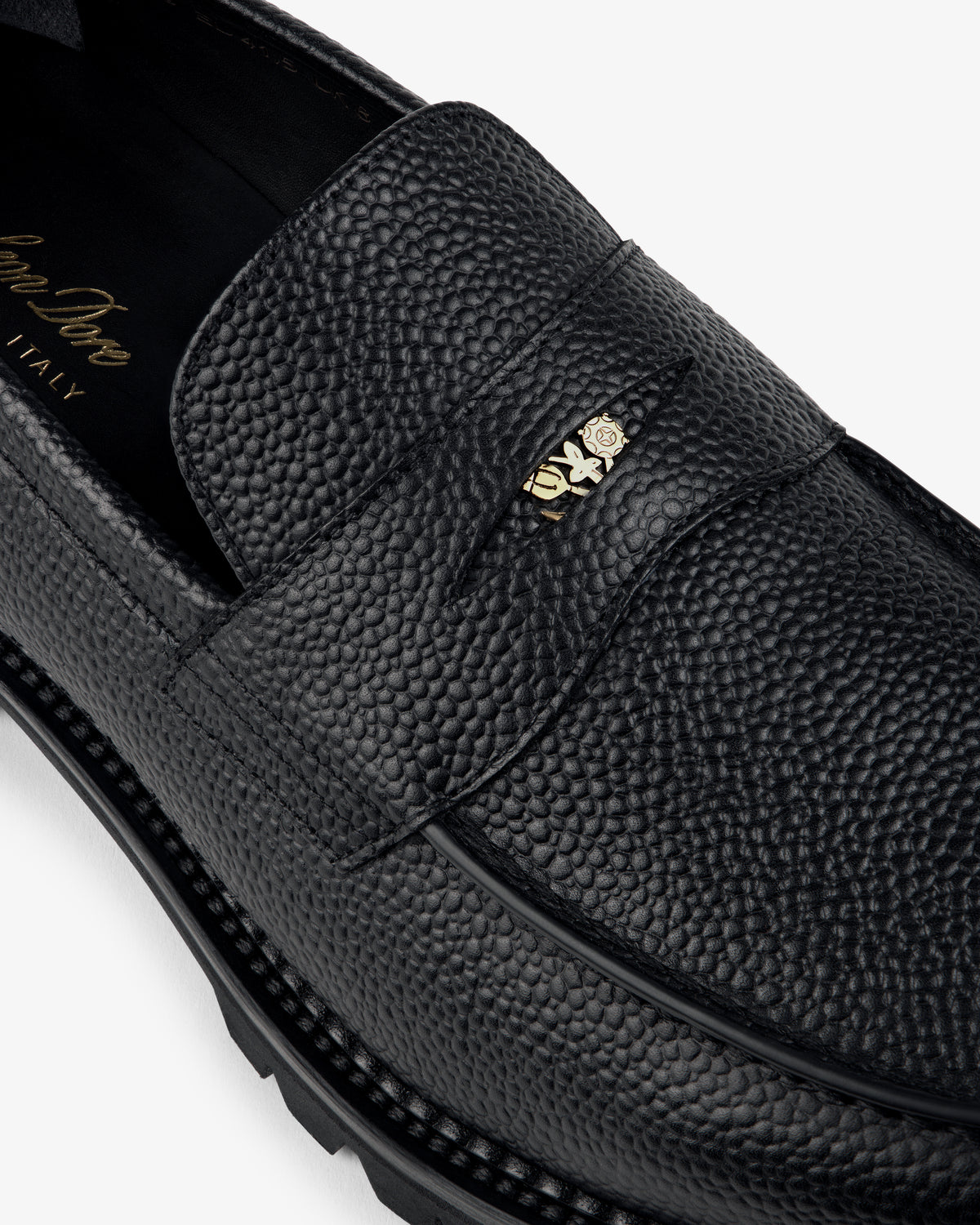 Close-up of the Lug Sole Queens Crest Loafer in black textured leather with a gold-tone metal strap detail.