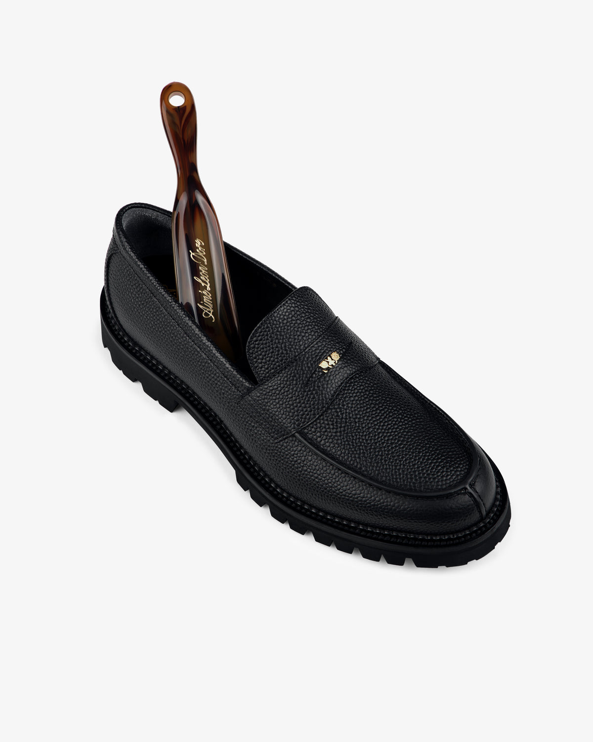 Lug Sole Queens Crest Loafer in black leather with a gold logo and brown tortoiseshell shoehorn on a white background.