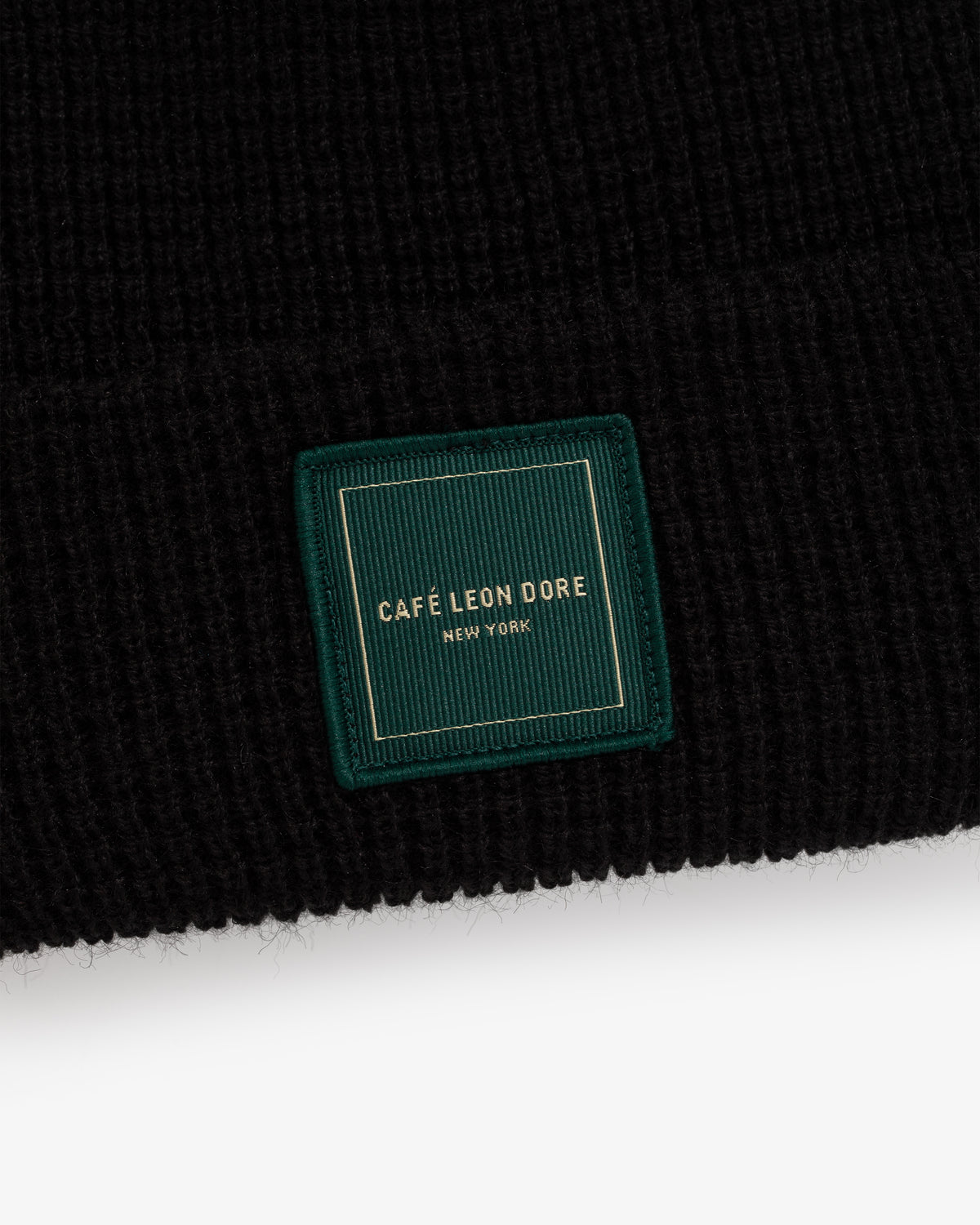 Café Leon Dore Beanie: black knit hat with a green patch, gold “CAFÉ LEON DORE NEW YORK” embroidery.