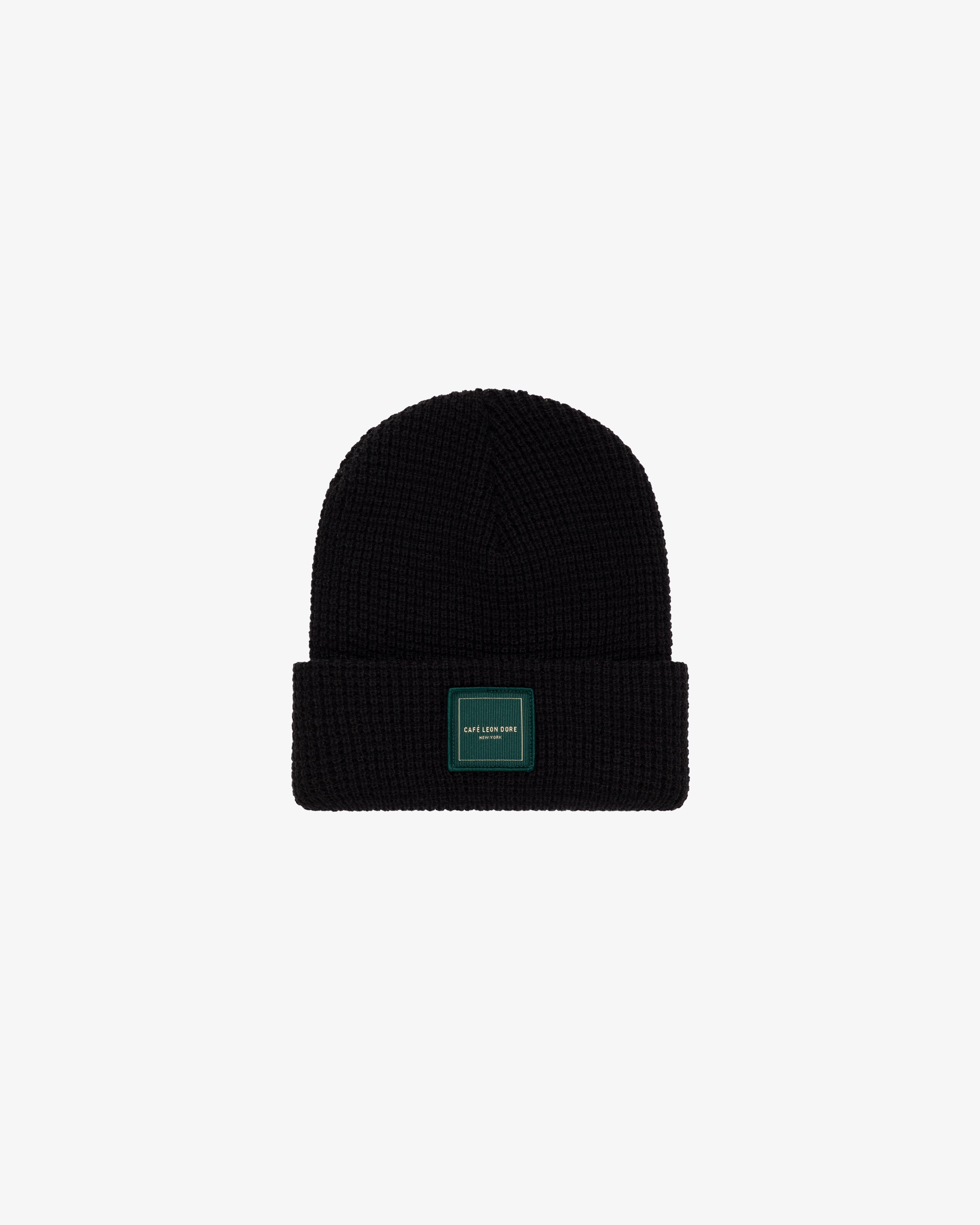 Café Leon Dore Beanie: black knit with folded brim and rectangular green patch, shown on a white background.