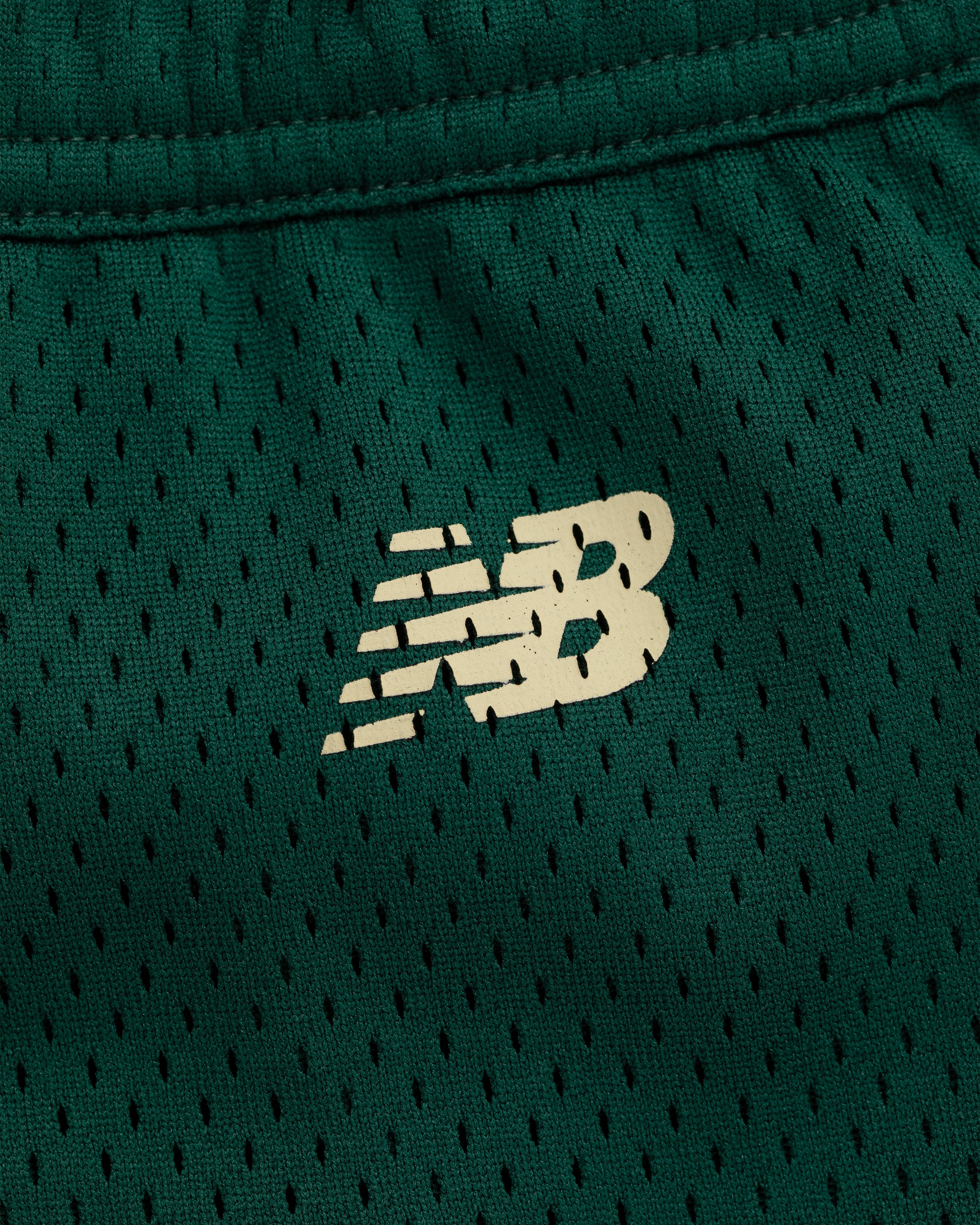 Close-up of a white New Balance logo on green mesh ALD / New Balance SONNY NY Gym Short.