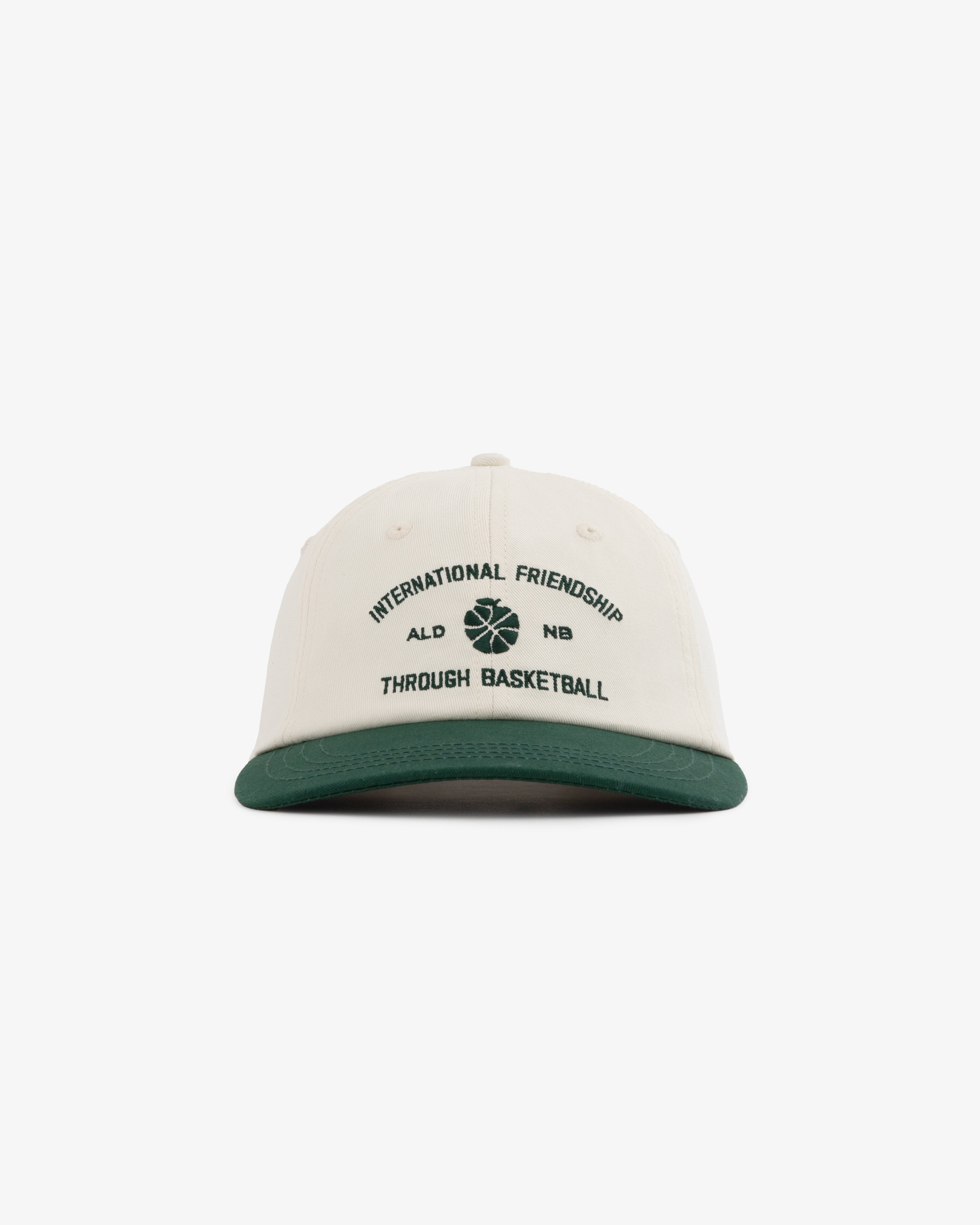 ALD / New Balance SONNY NY IFTB Hat: white cap, green brim, "International Friendship Through Basketball" text, basketball graphic.