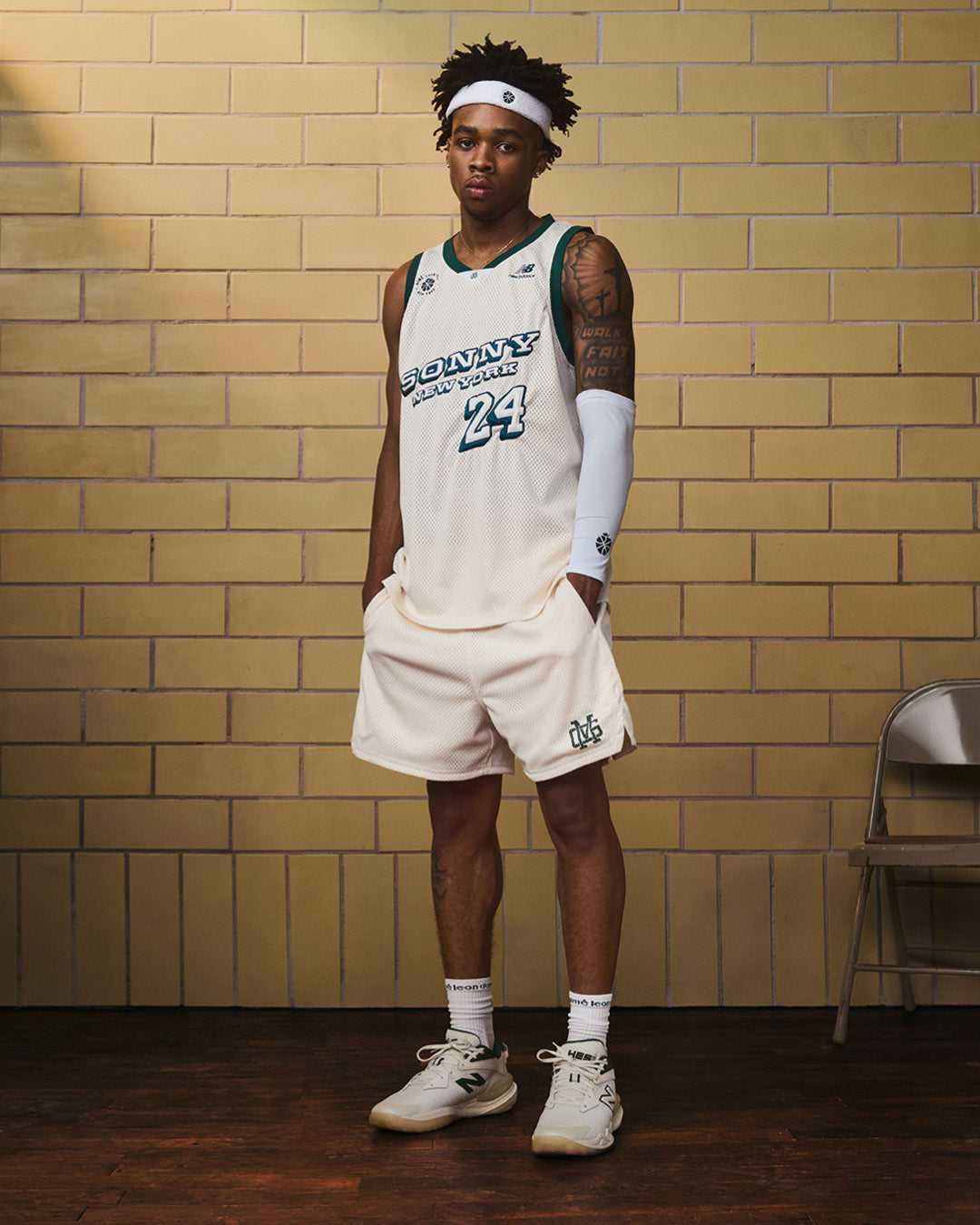 A basketball player in ALD / New Balance SONNY NY Gym Shorts stands indoors by a folding chair, looking at the camera.
