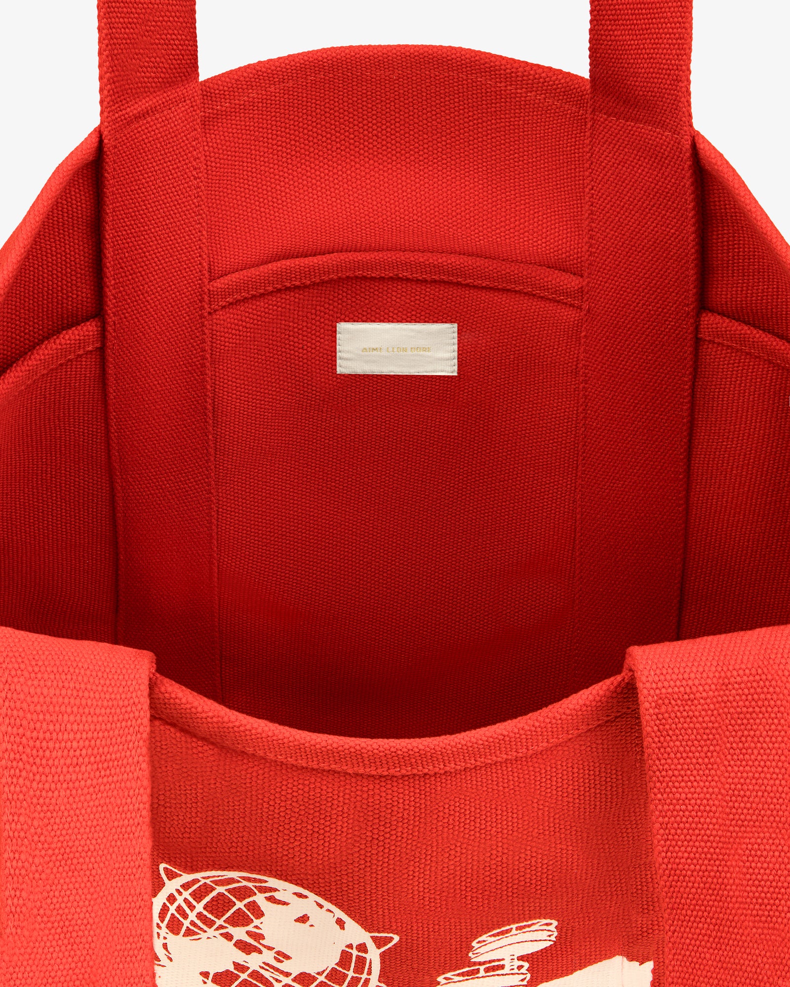 Large Unisphere Tote Bag has a red interior, white graphic partially visible outside, label inside, and sturdy handles.