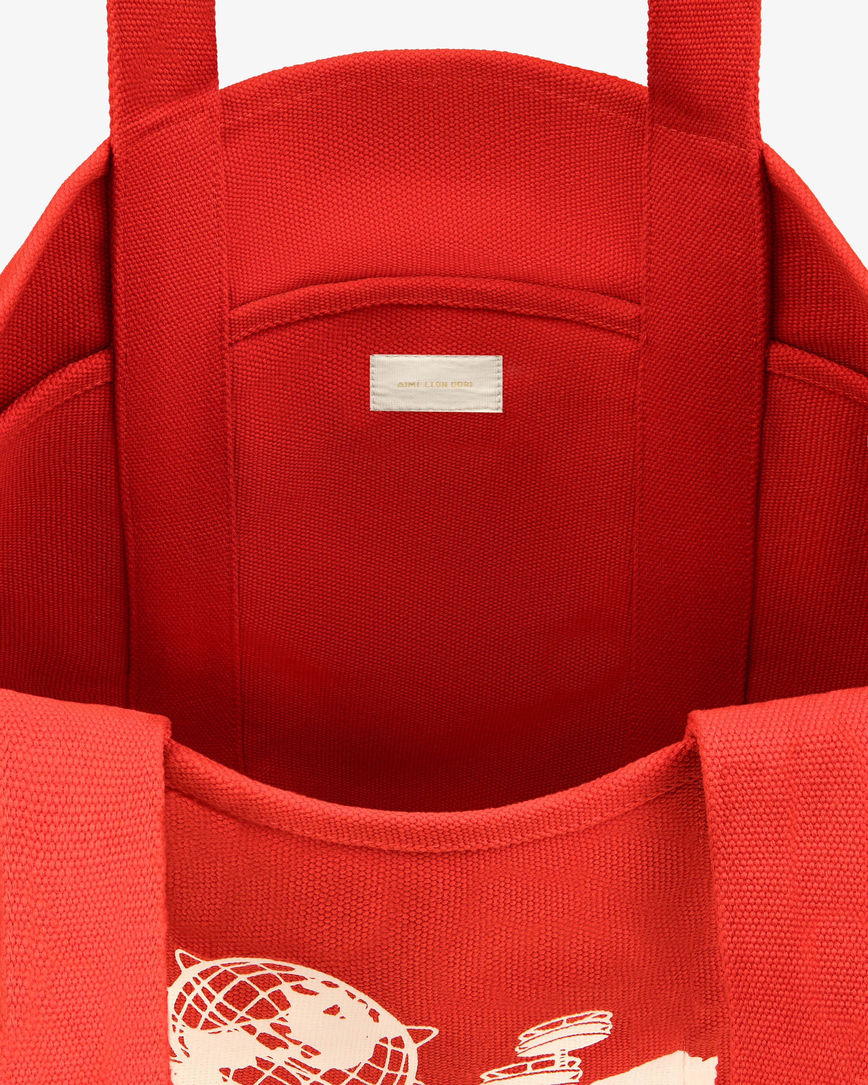 Large Unisphere Tote Bag has a red interior, white graphic partially visible outside, label inside, and sturdy handles.