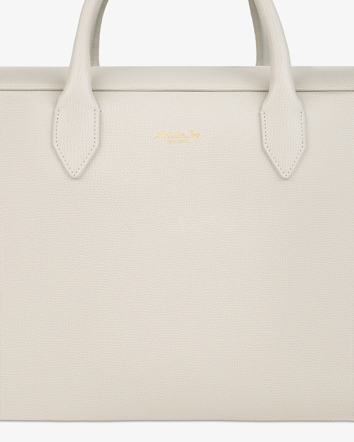 Close-up of a textured, off-white Full Grain Leather Briefcase Duffle with two handles and a small gold logo in the center.
