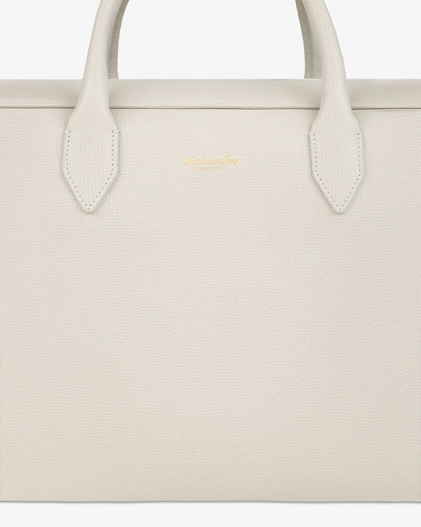 Close-up of a textured, off-white Full Grain Leather Briefcase Duffle with two handles and a small gold logo in the center.