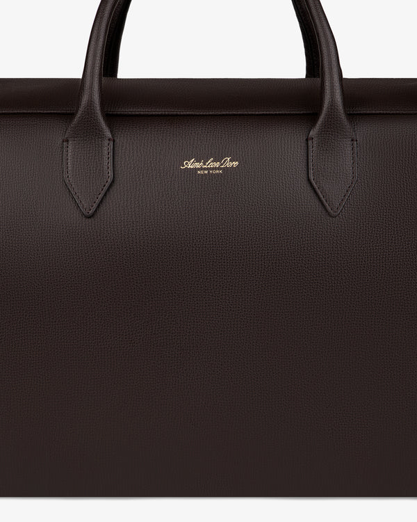 Close-up of a dark brown Full Grain Leather Briefcase Duffle with two handles and gold Mark Cross New York logo.