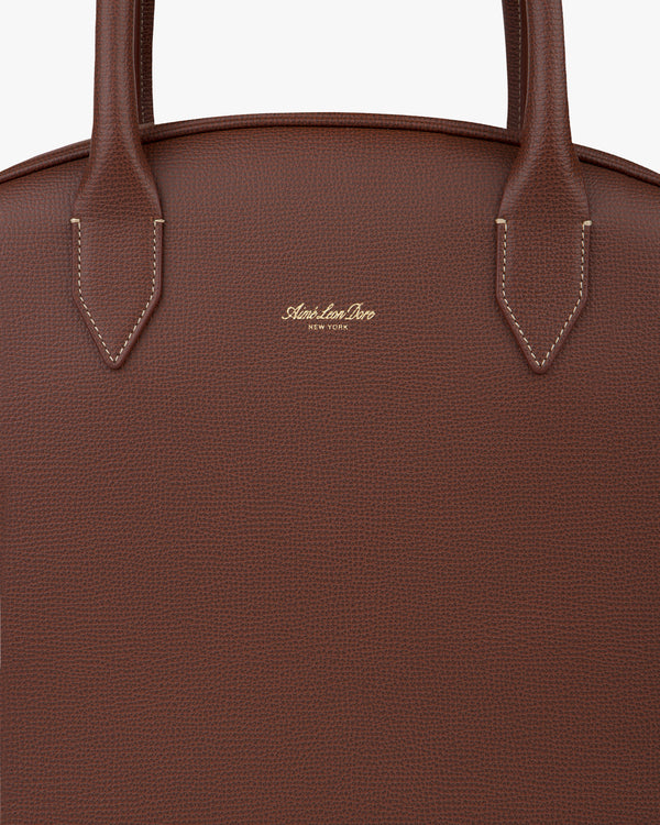 Close-up of Full Grain Leather Crescent Shoulder Bag in brown with two handles and gold embossed logo on the front.