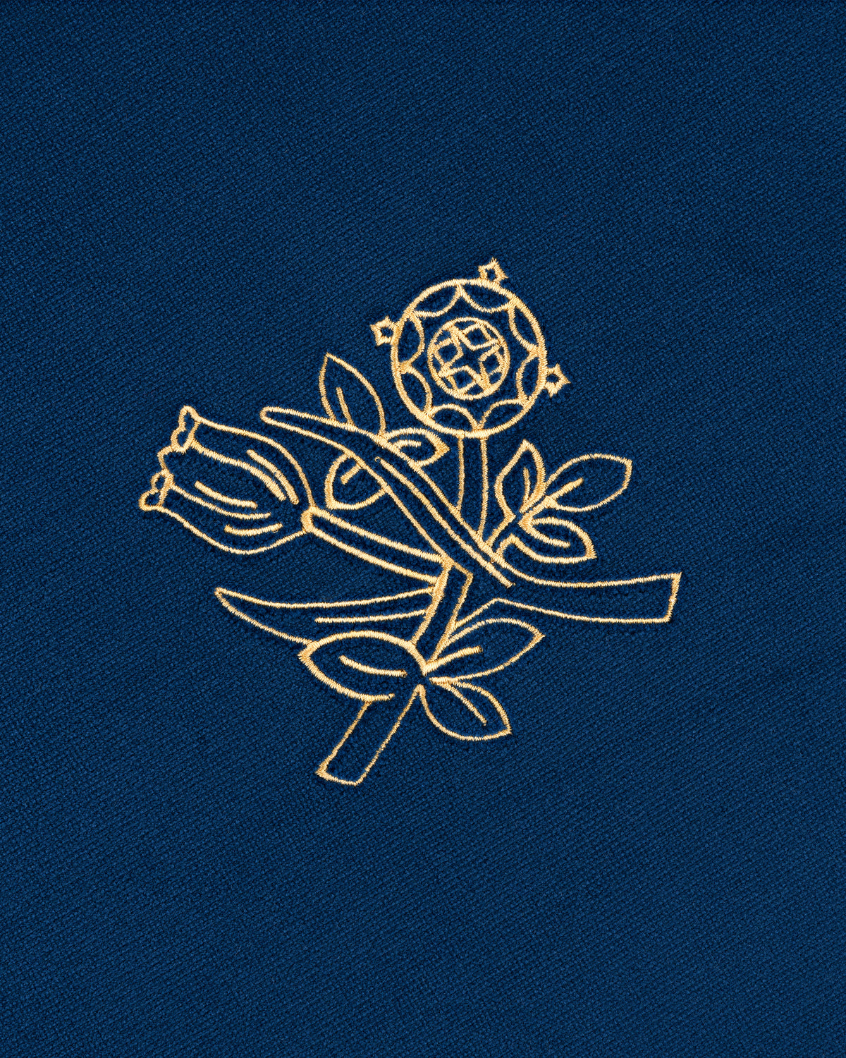 The Queens Crest Throw Pillow features gold floral embroidery on blue, with a rose, leaves, and geometric accents.