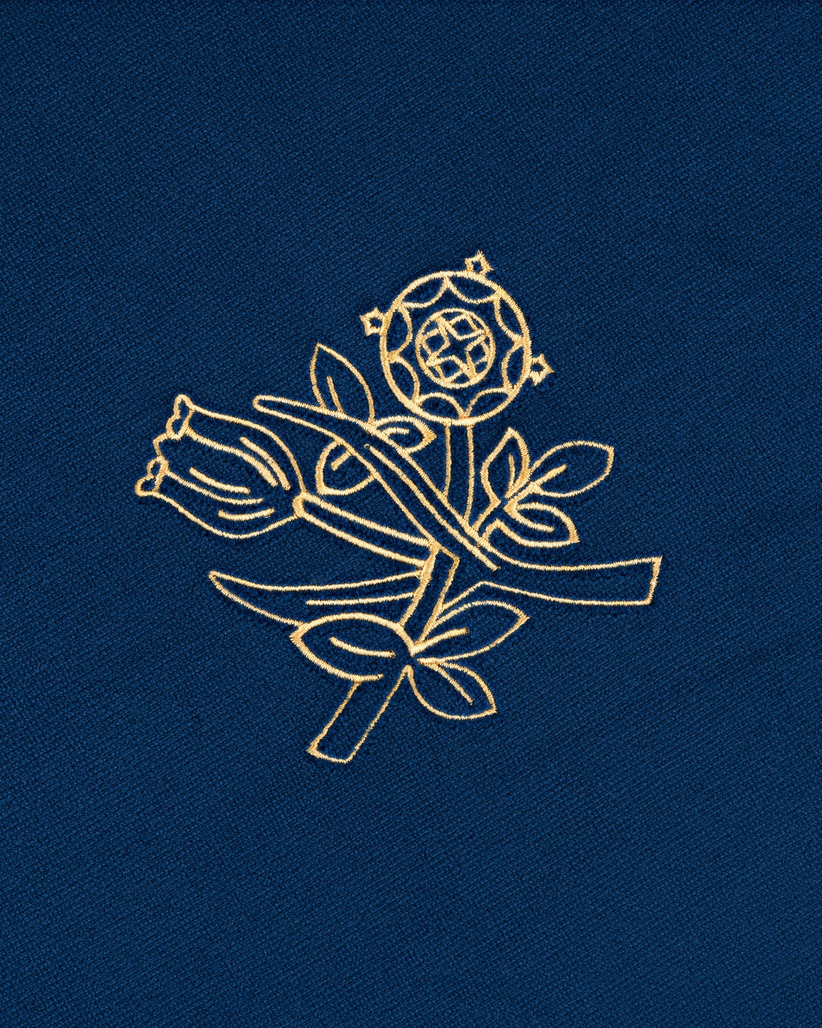 The Queens Crest Throw Pillow features gold floral embroidery on blue, with a rose, leaves, and geometric accents.