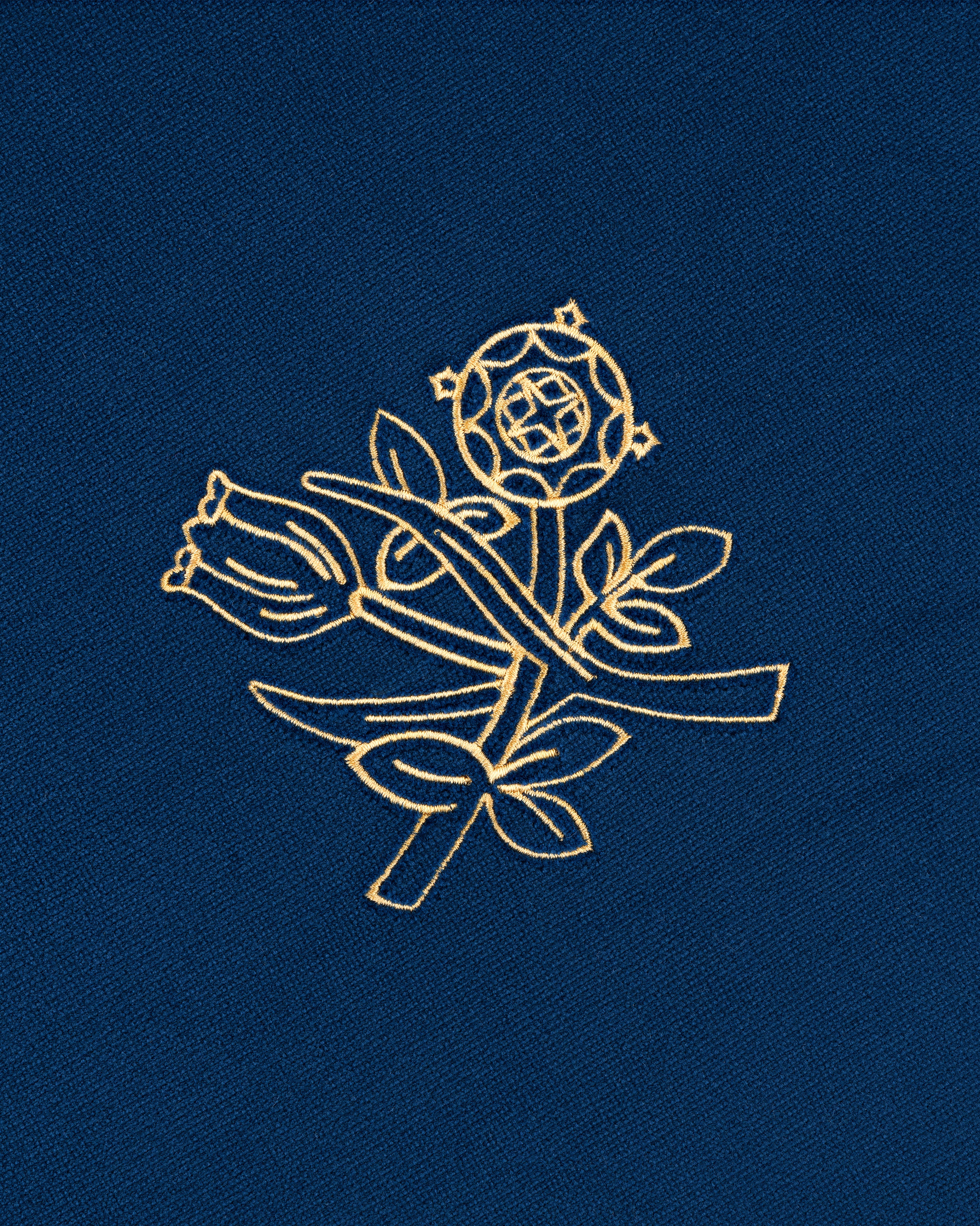 The Queens Crest Throw Pillow features gold floral embroidery on blue, with a rose, leaves, and geometric accents.