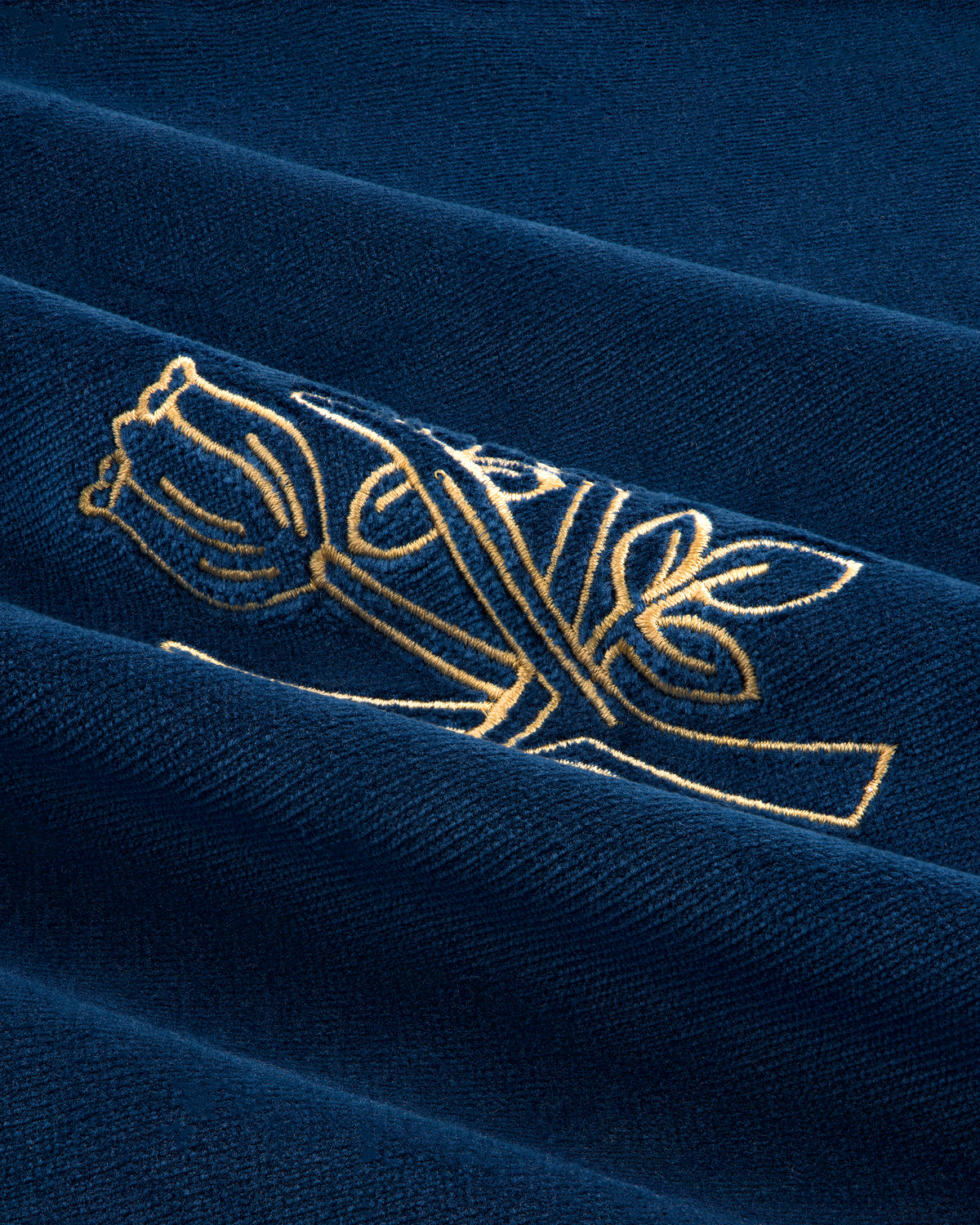 Queens Crest Throw Pillow features gold embroidered roses on dark blue fabric with textured folds.