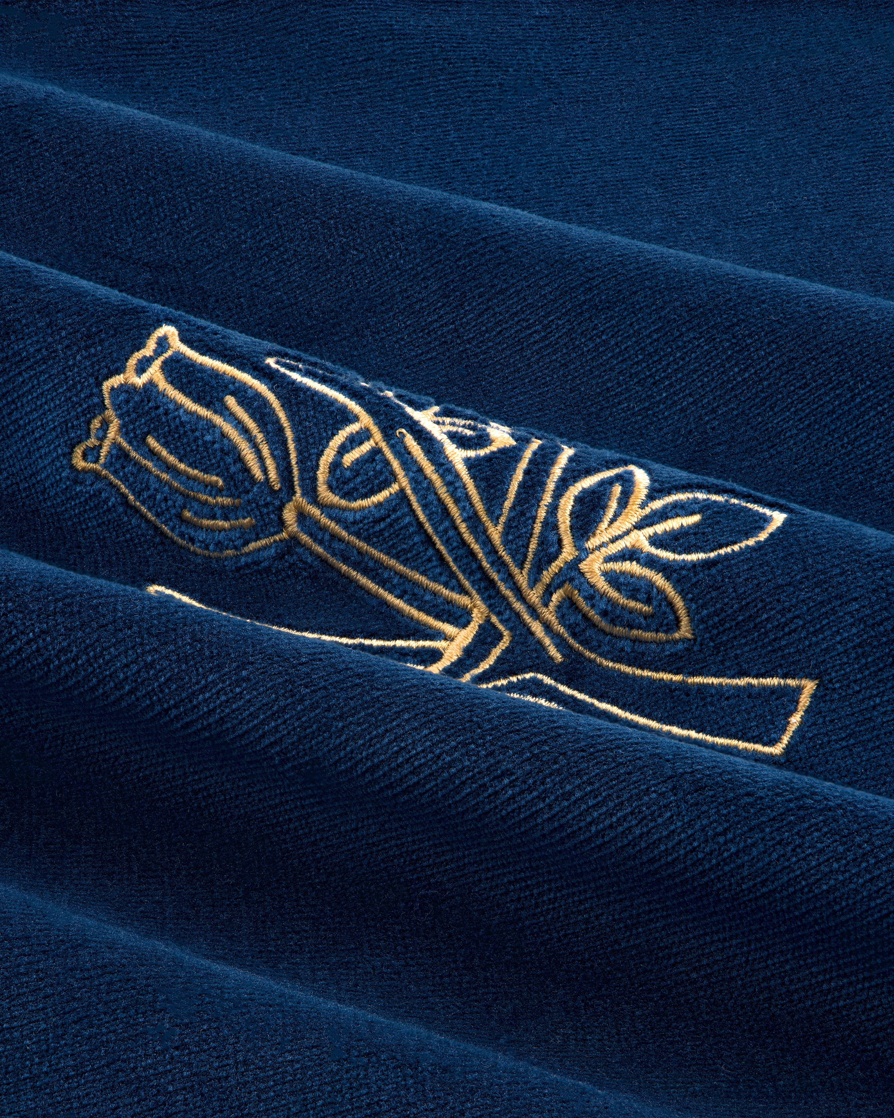 Queens Crest Throw Pillow features gold embroidered roses on dark blue fabric with textured folds.