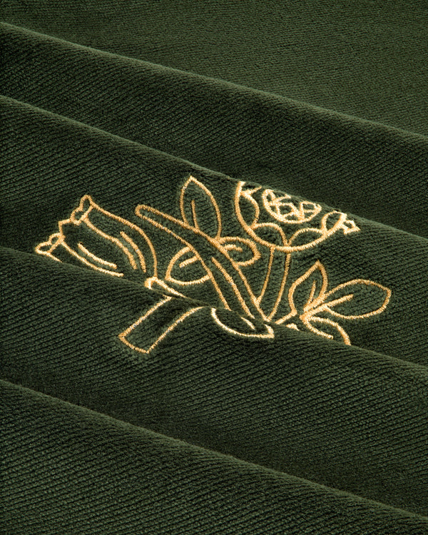 Close-up of the Queens Crest Throw Pillow's green fabric with two flowers and leaves embroidered in light yellow thread.