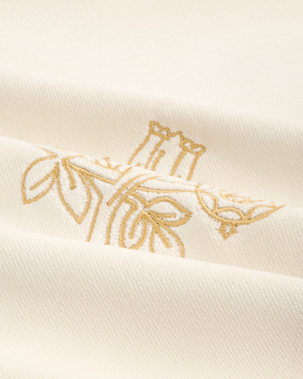 Queens Crest Throw Pillow: White fabric with gold floral embroidery and a soft, textured finish.