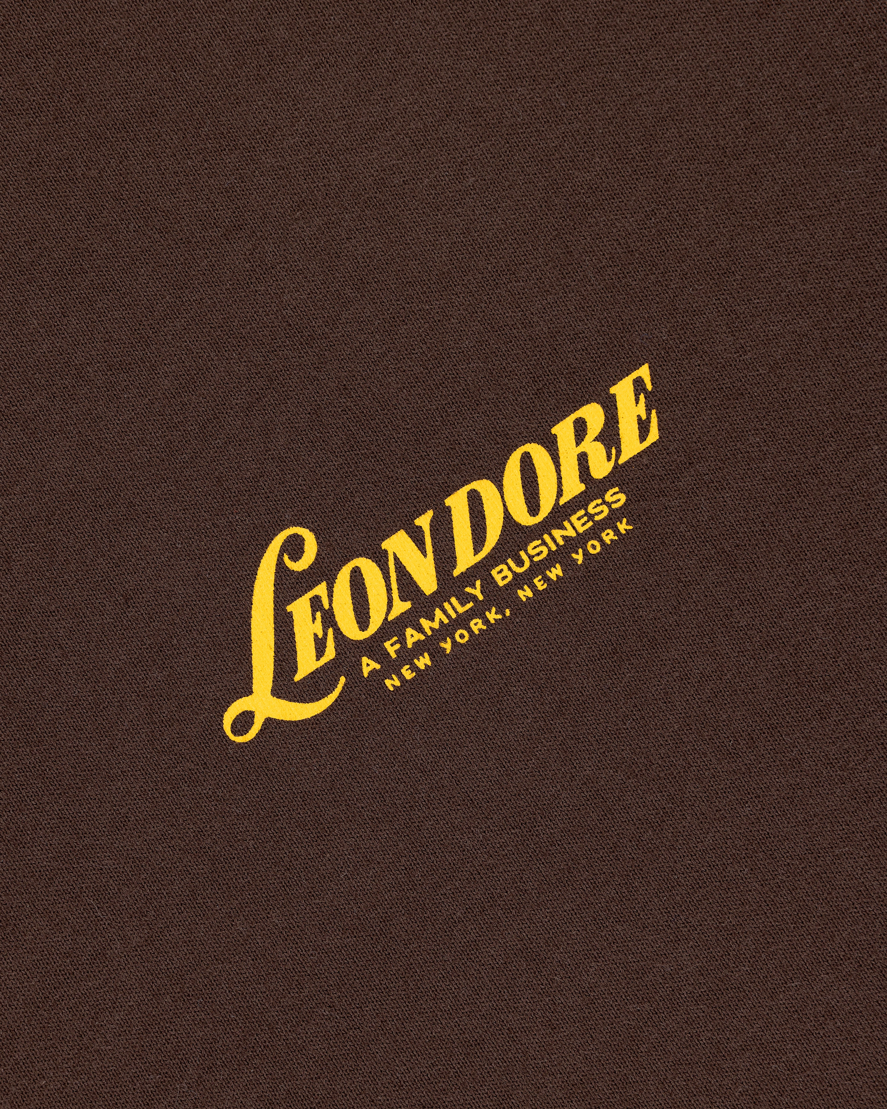 Yellow "LEON DORE, A FAMILY BUSINESS, NEW YORK, NEW YORK" text on brown textured Leon Dore Tee.