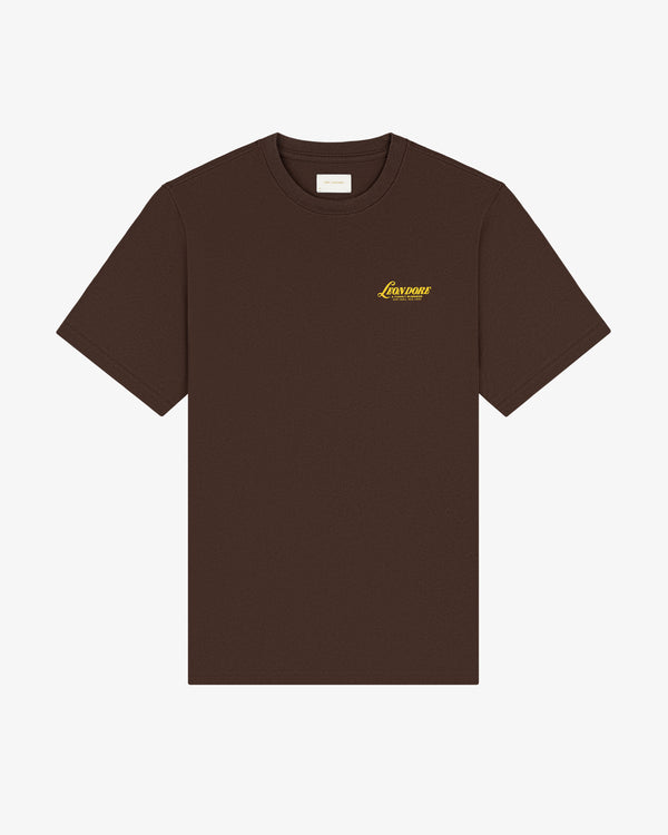 Brown Leon Dore Tee with short sleeves and small yellow Lowtone logo on left chest, shown on white background.