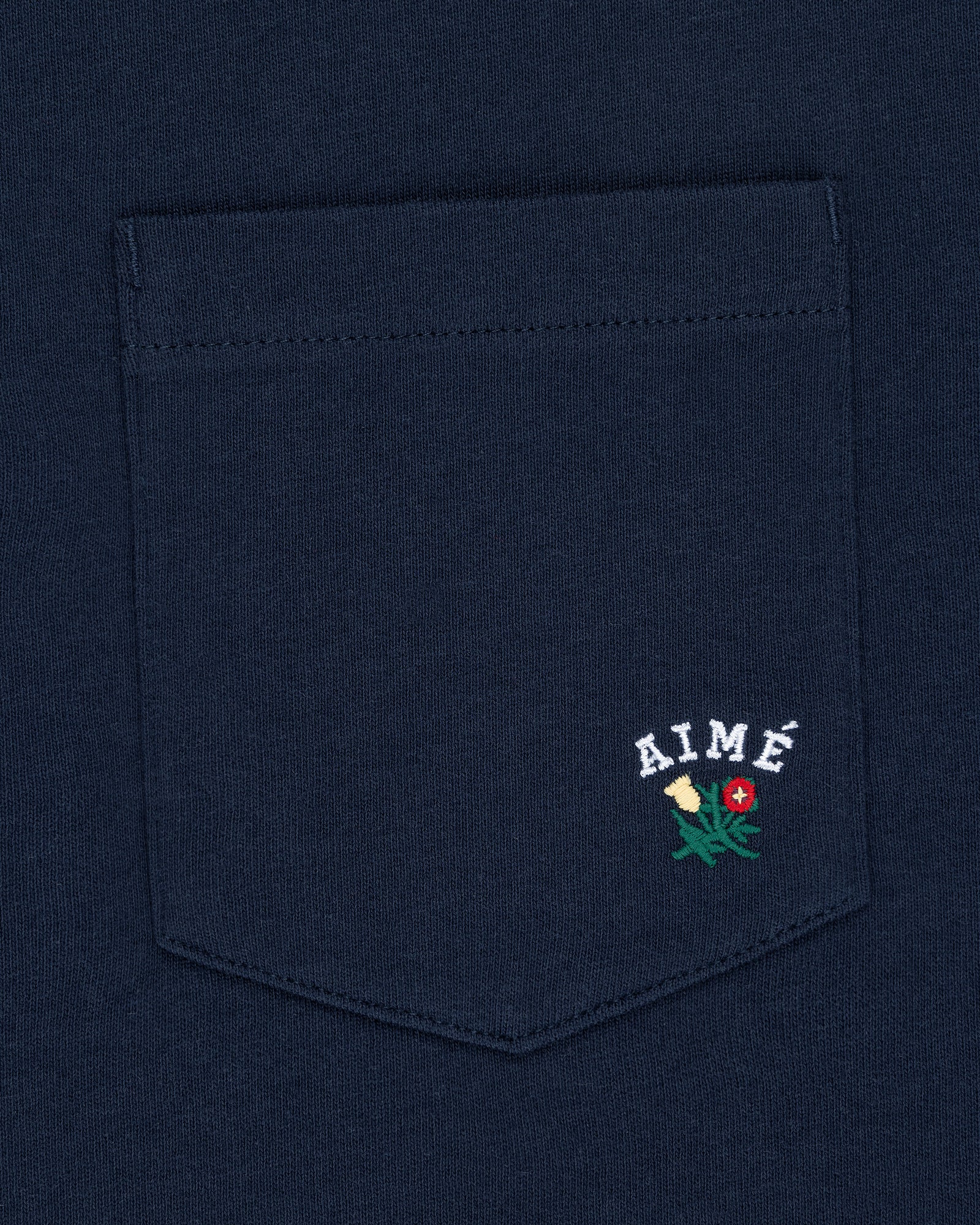 Navy Crest Pocket Tee with “AIMÉ” text and small embroidered flower design below the lettering.