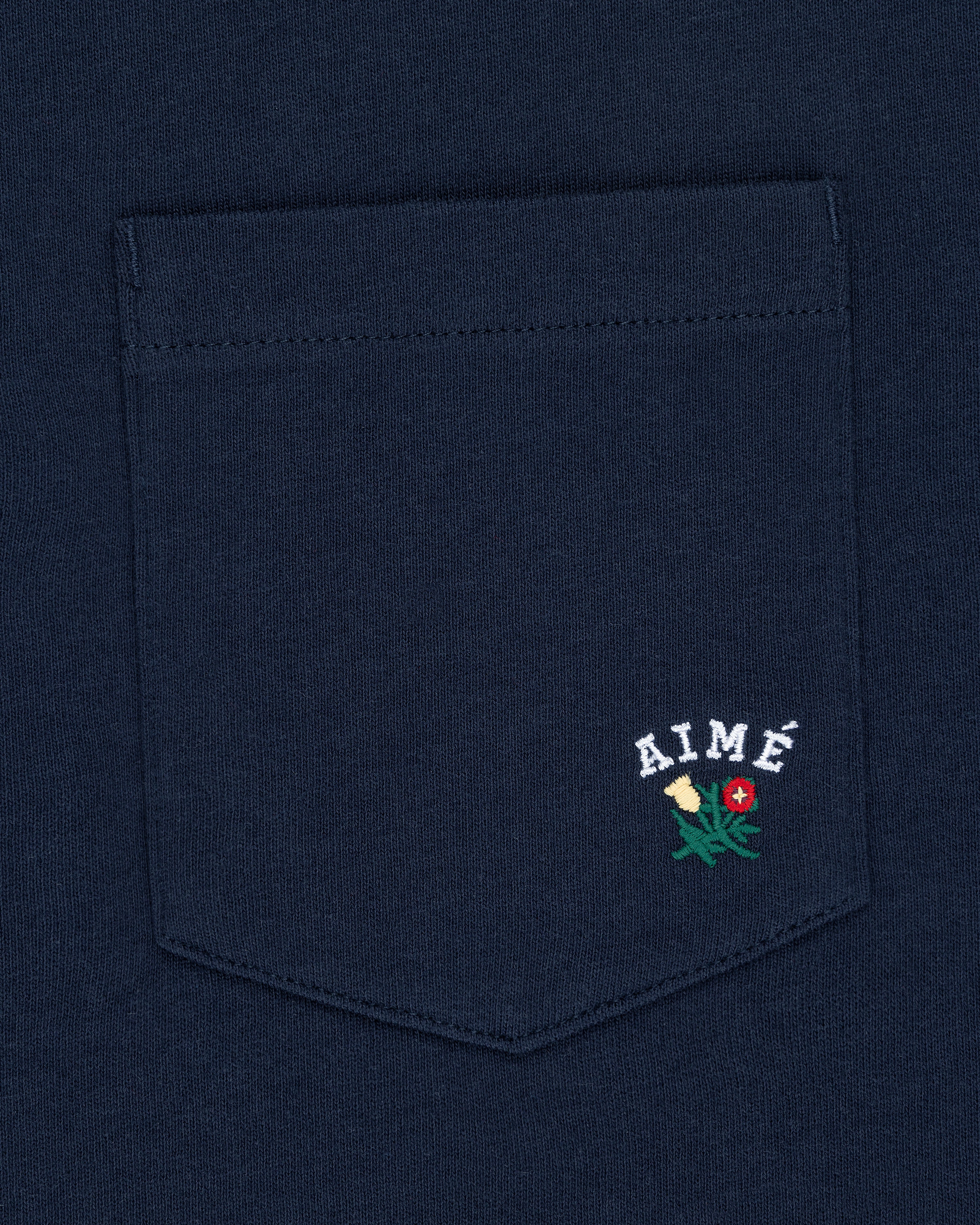 Navy Crest Pocket Tee with “AIMÉ” text and small embroidered flower design below the lettering.