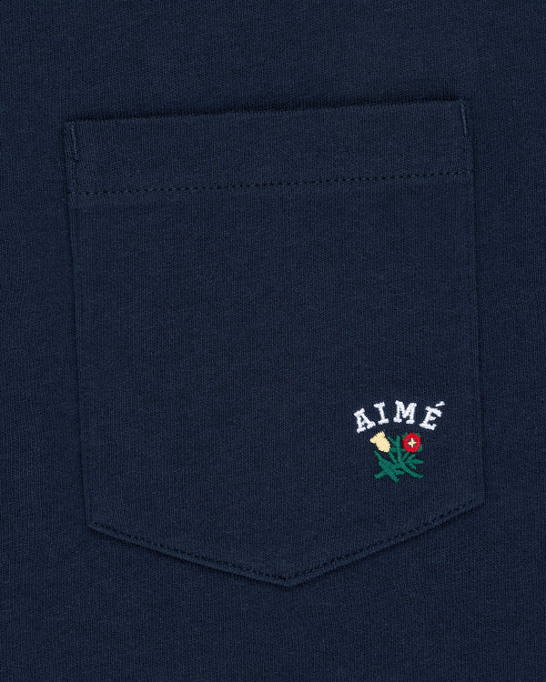 Navy Crest Pocket Tee with “AIMÉ” text and small embroidered flower design below the lettering.