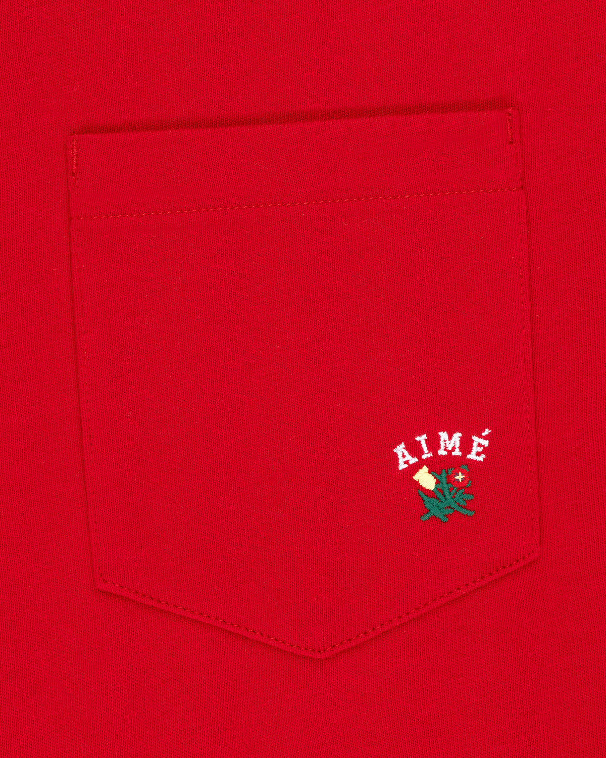 Crest Pocket Tee: Red tee with white AIMÉ text and a small green and yellow flower embroidered below.