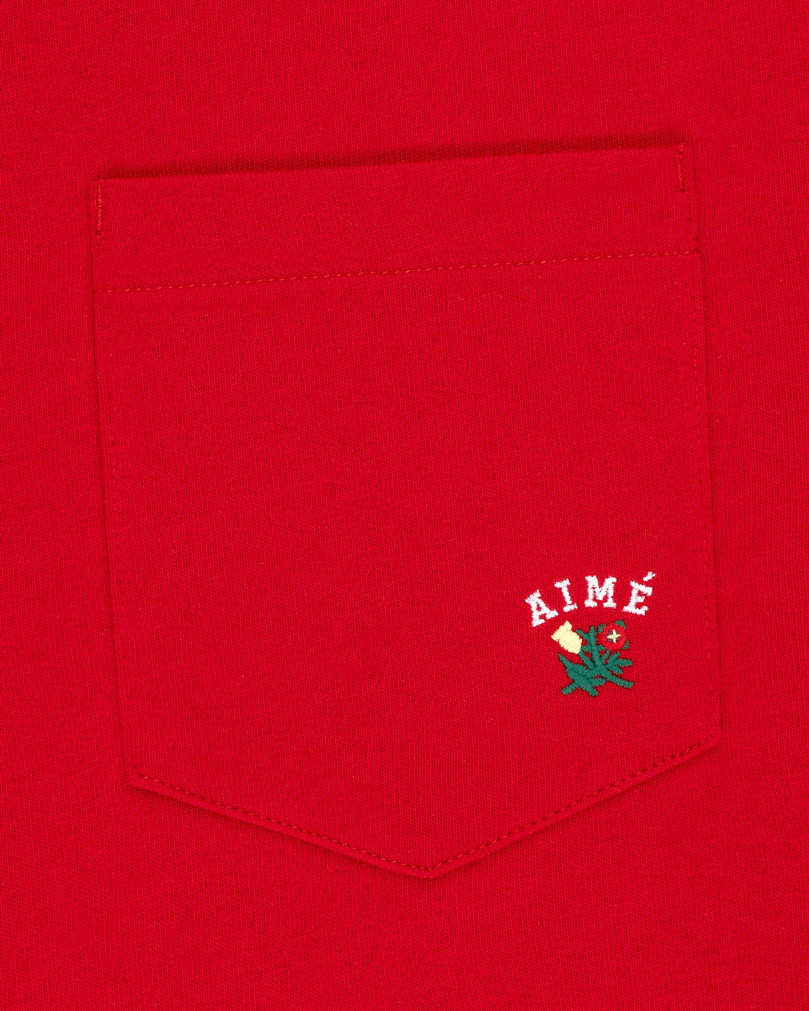 Crest Pocket Tee: Red tee with white AIMÉ text and a small green and yellow flower embroidered below.