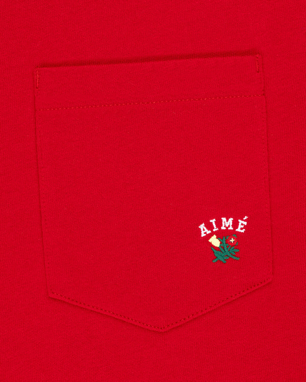 Crest Pocket Tee: Red tee with white AIMÉ text and a small green and yellow flower embroidered below.