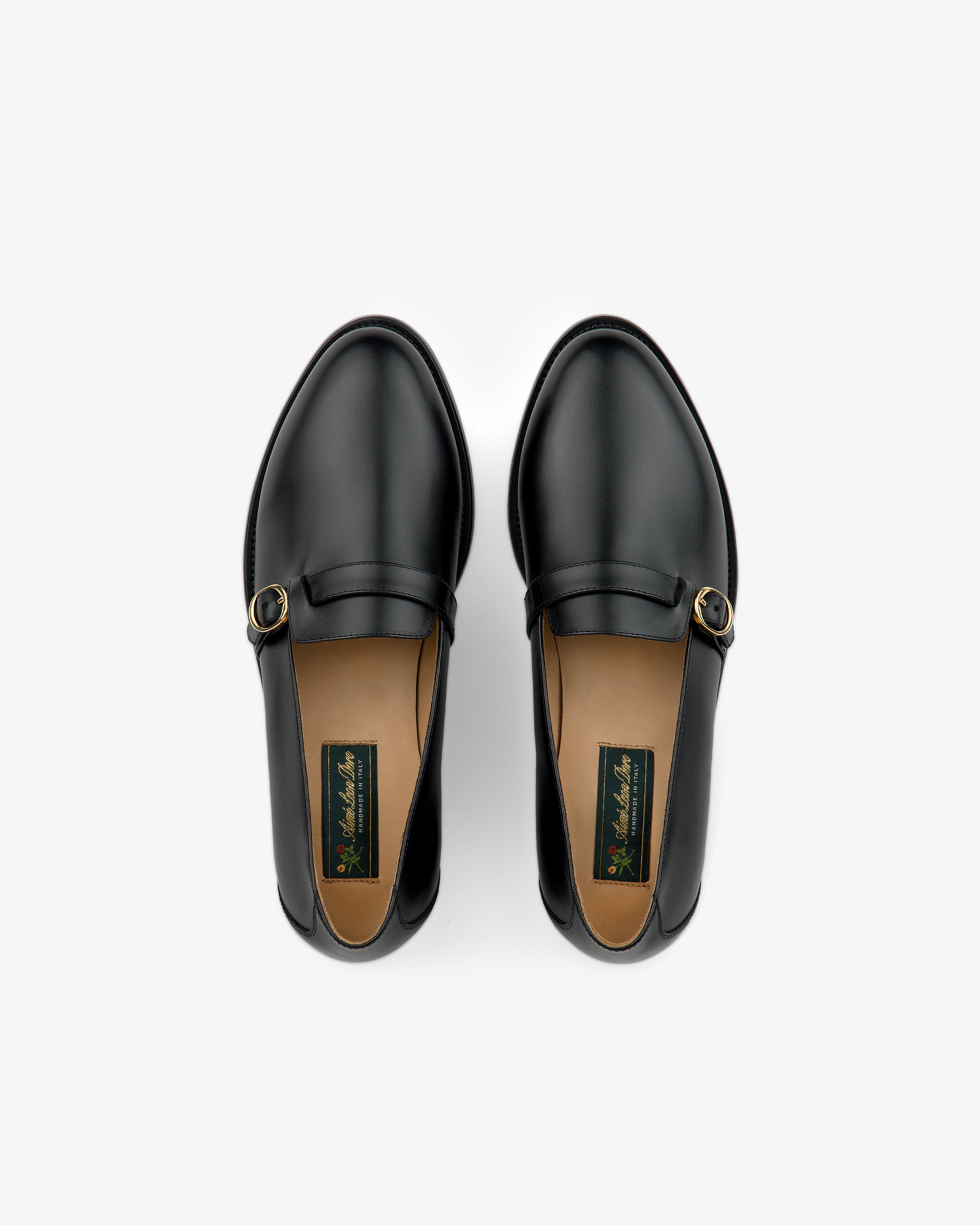 Venetian Buckle Loafers in black leather with gold buckles, top view on a white background.