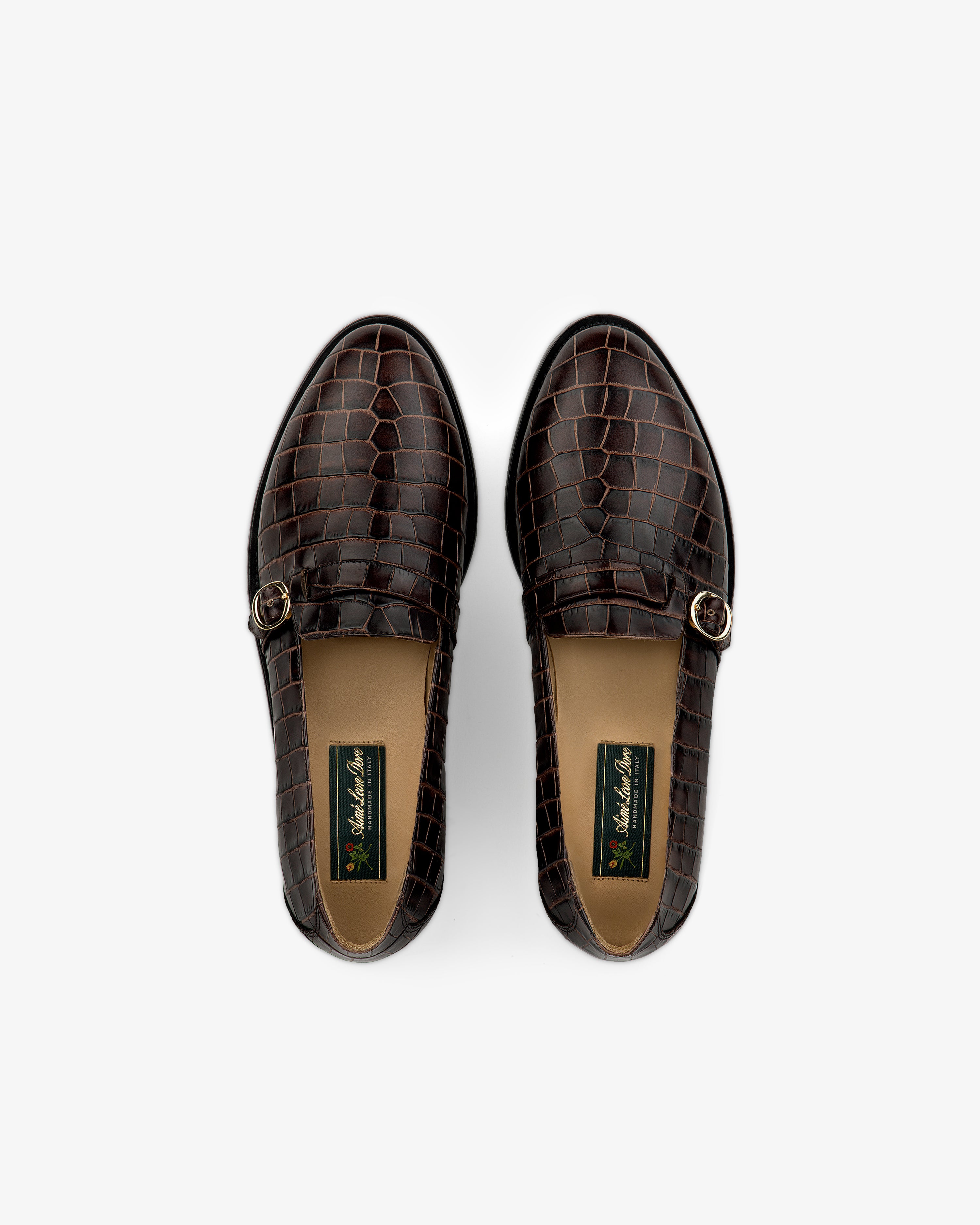Venetian Croc Buckle Loafers in brown, crocodile-patterned leather with buckles, top view on white background.