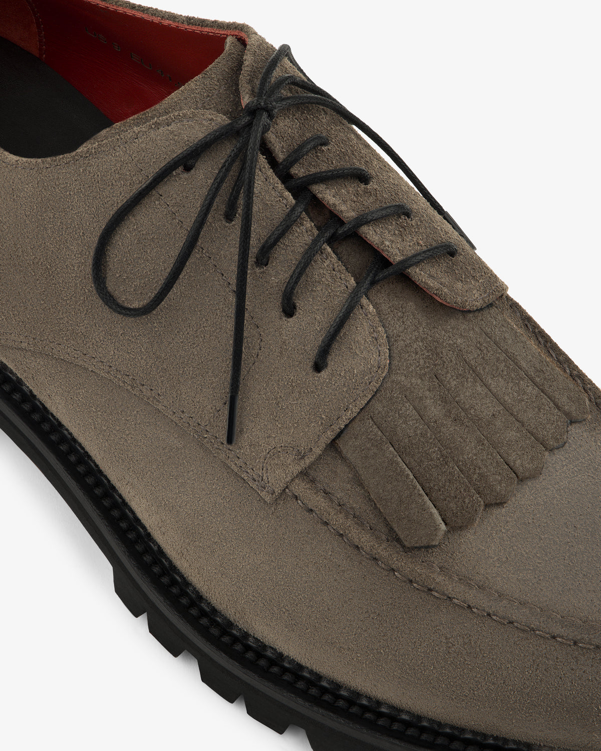 Close-up of the Suede Lug Sole Derby in taupe suede with black laces and fringe, shown on a white background.
