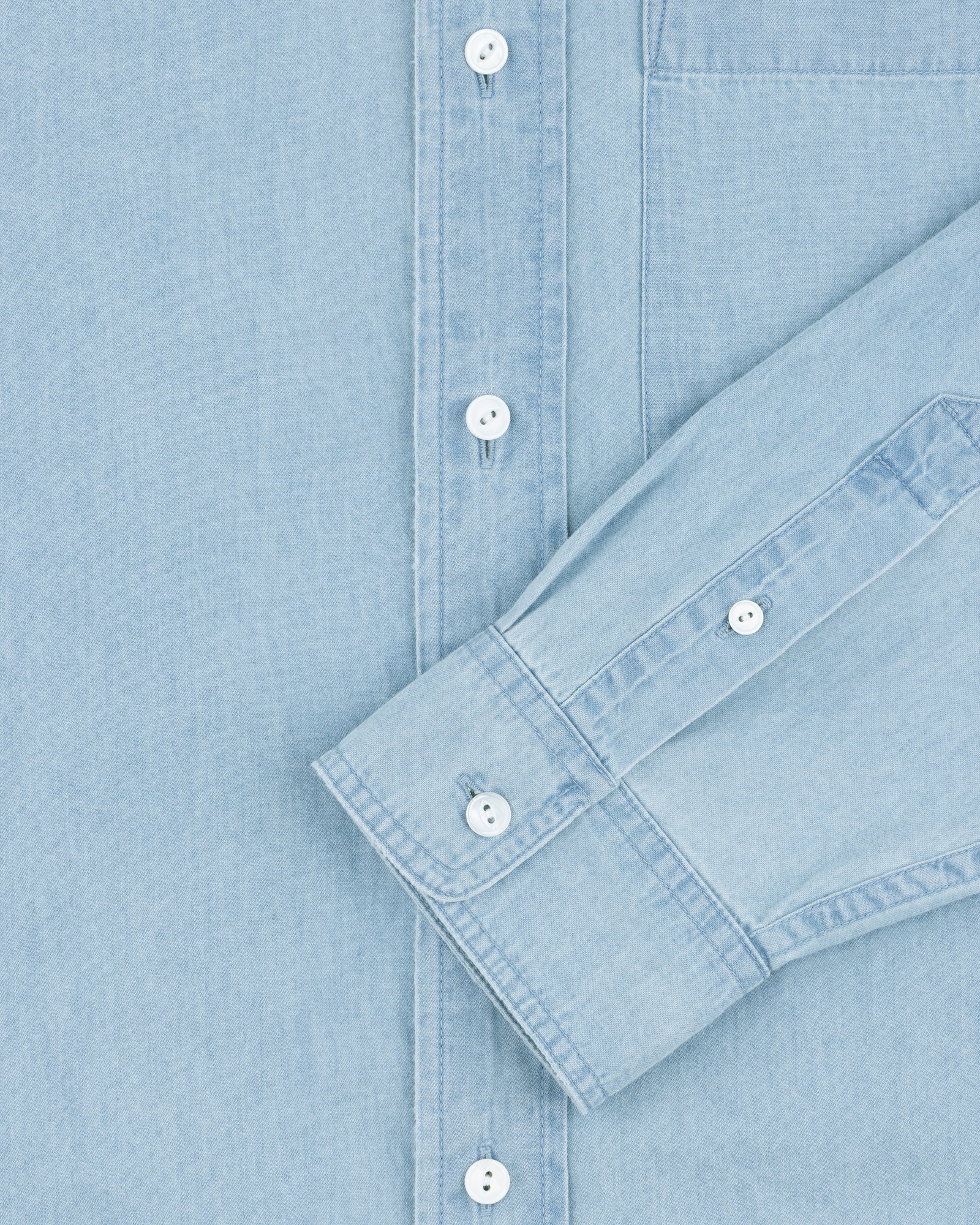 Denim Collarband Shirt in light blue with white buttons, front view, one sleeve folded across the chest.