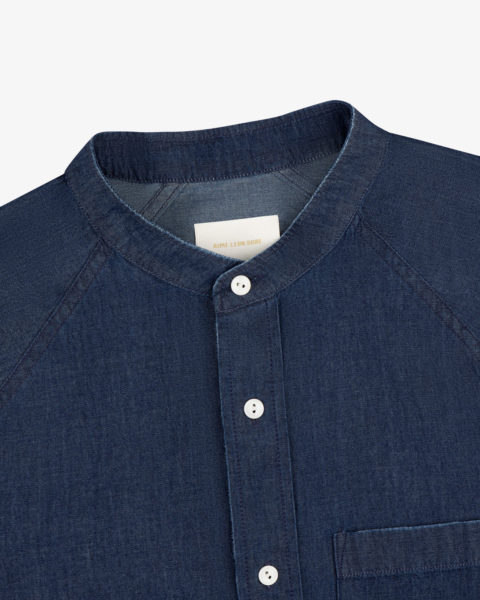 Denim Collarband Shirt in dark blue with white buttons, front pocket, and internal white neck label.